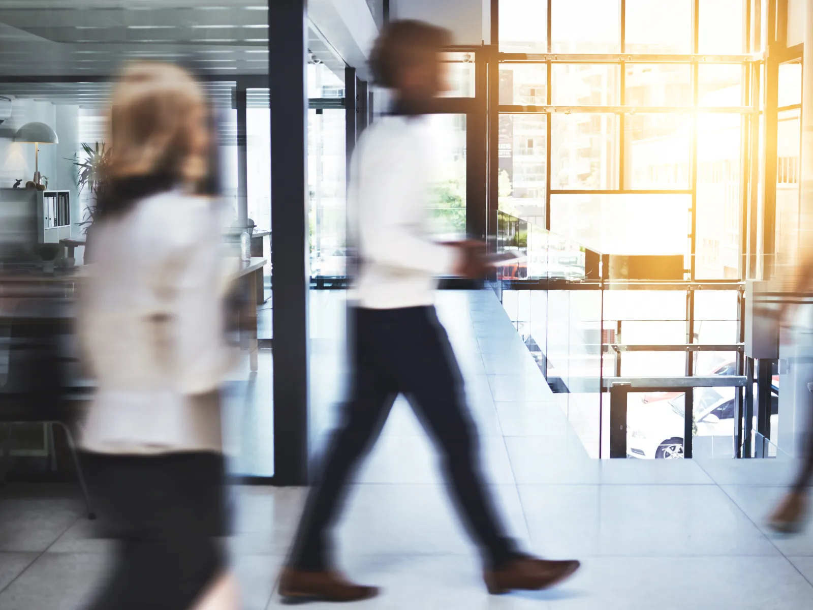 Blurred motion of business people walking inside a modern office building with large windows and natural light