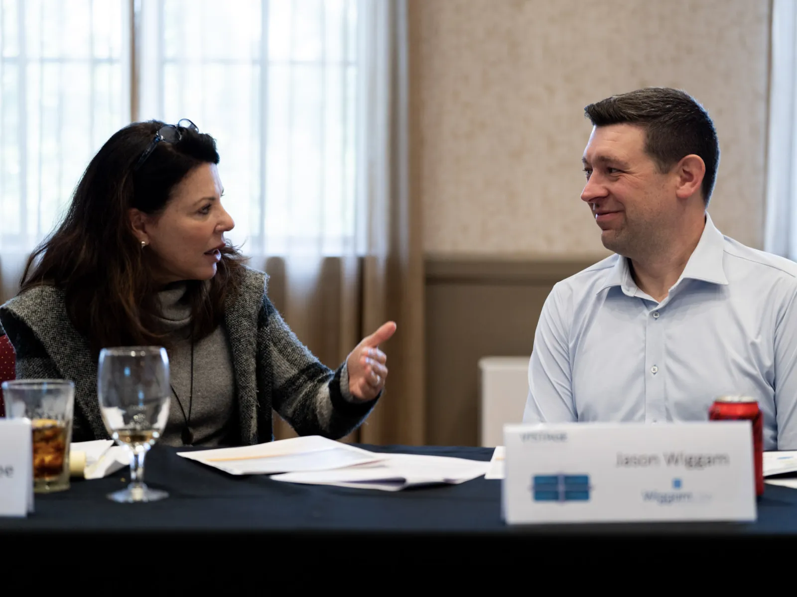Two professionals engaged in a conversation at a conference table with name tags and documents.