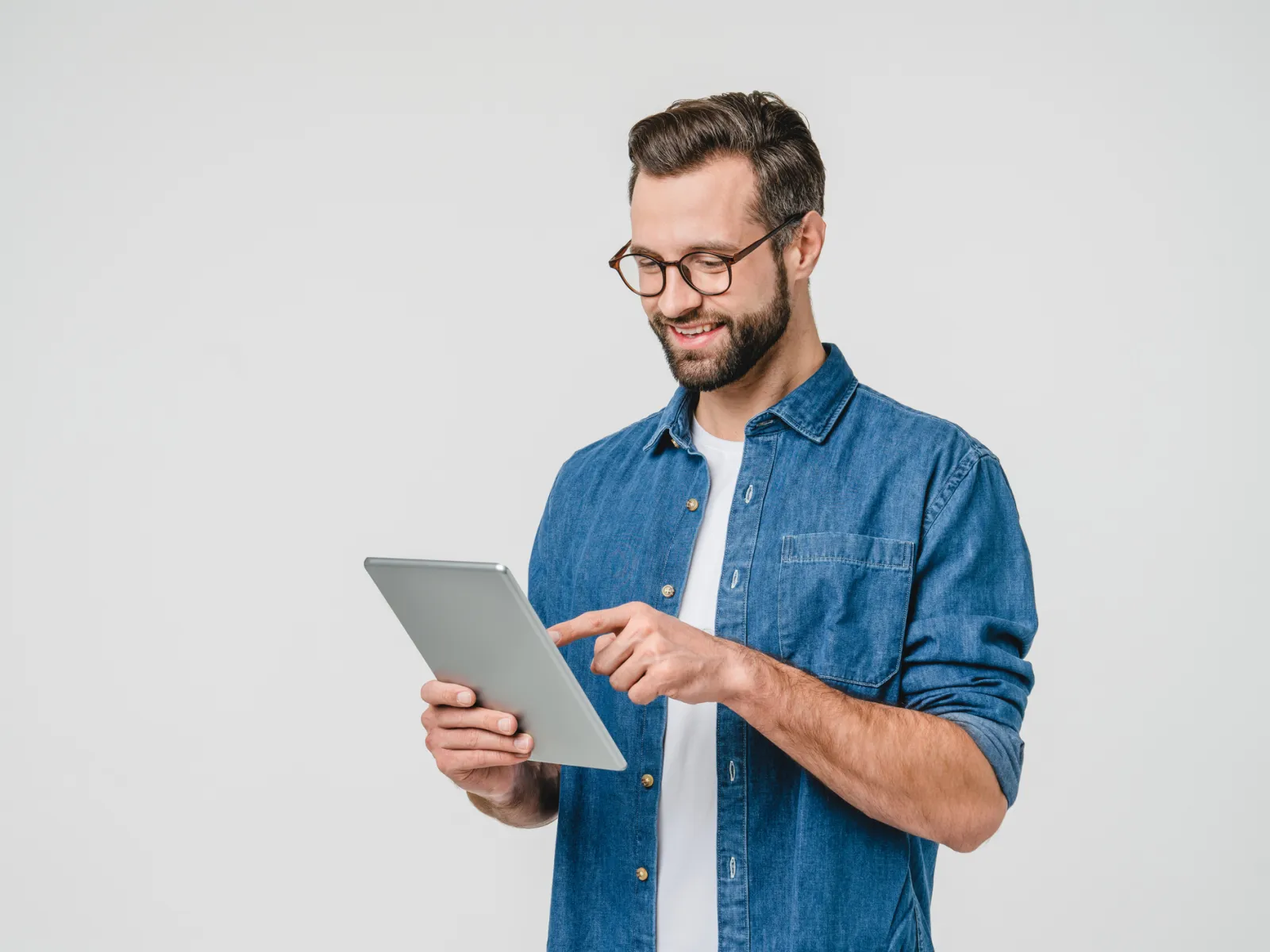 Smiling man in glasses using a tablet while standing against a plain white background