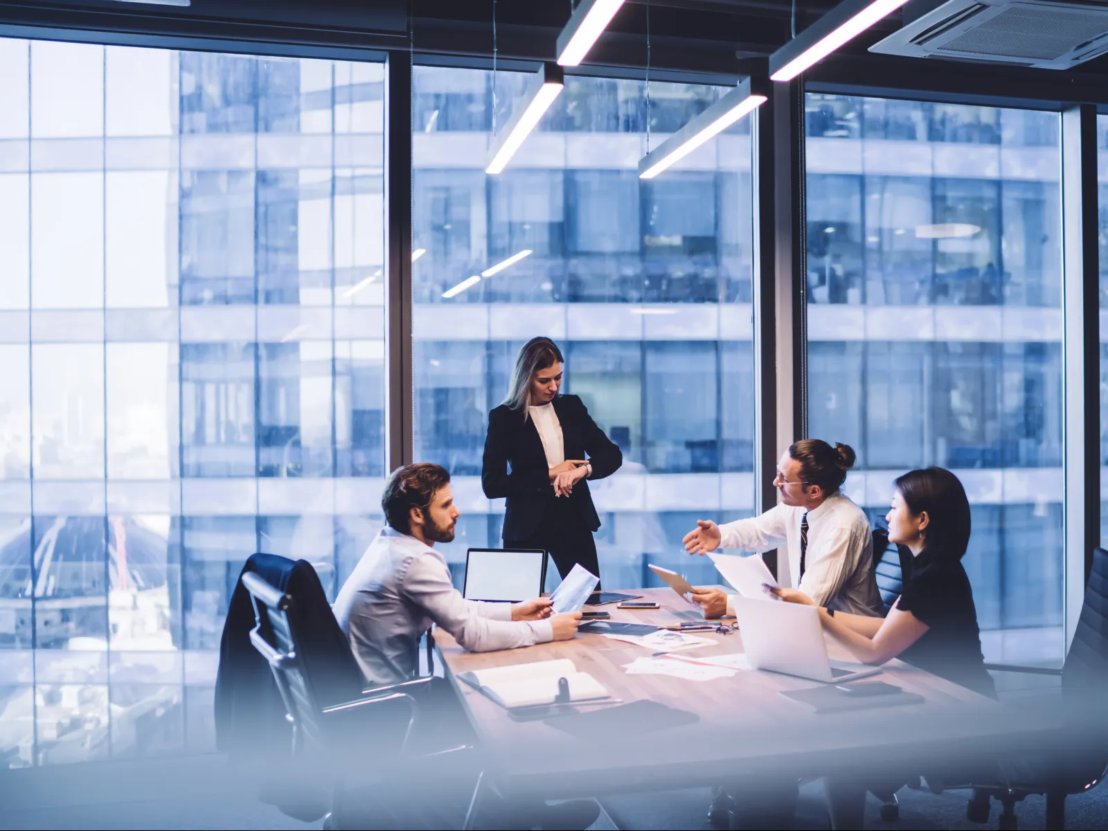 Business team discussing ideas in a modern office with floor-to-ceiling windows overlooking city buildings.