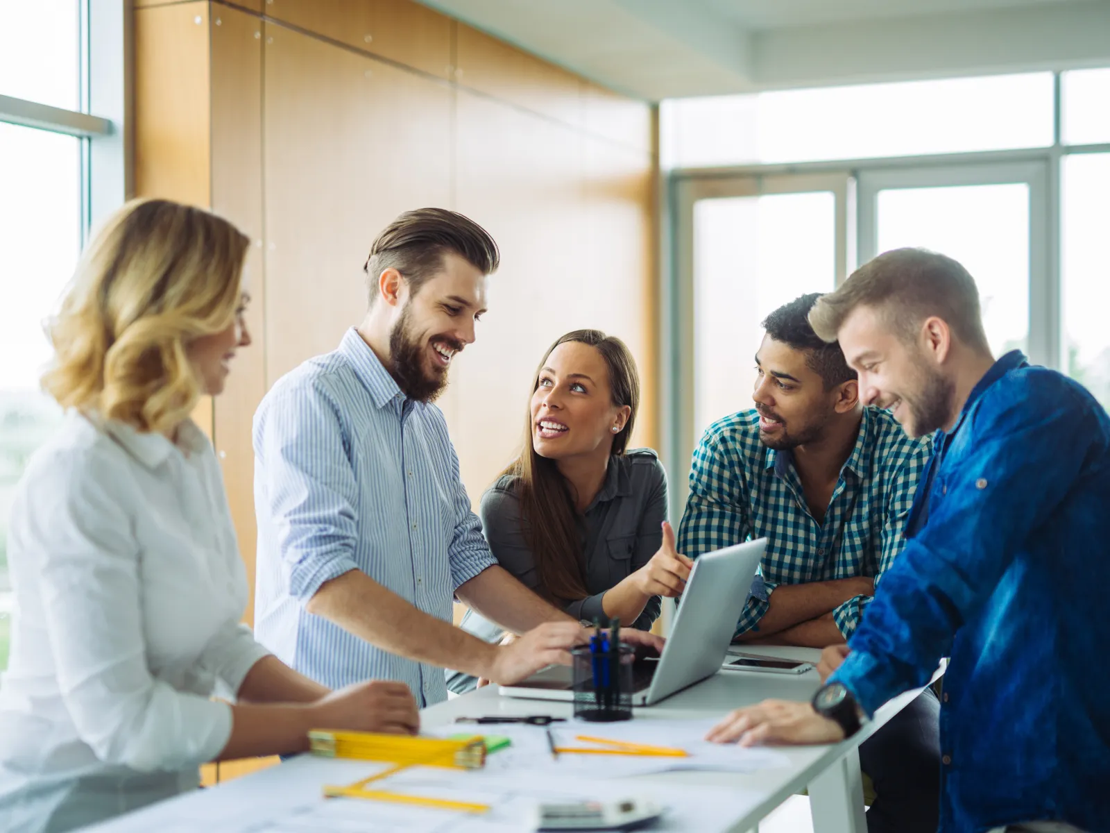Group of young professionals collaborating around a laptop in a bright modern office space.
