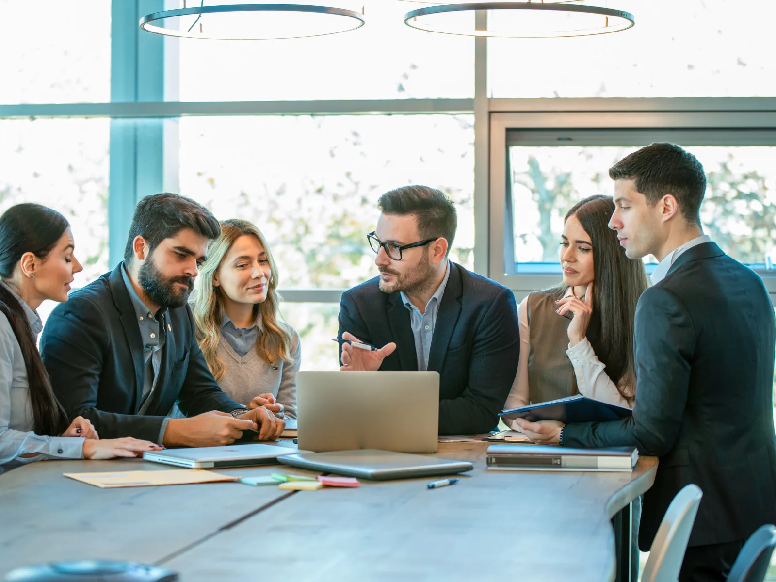 Five business professionals engaged in a meeting around a laptop in a bright modern office.