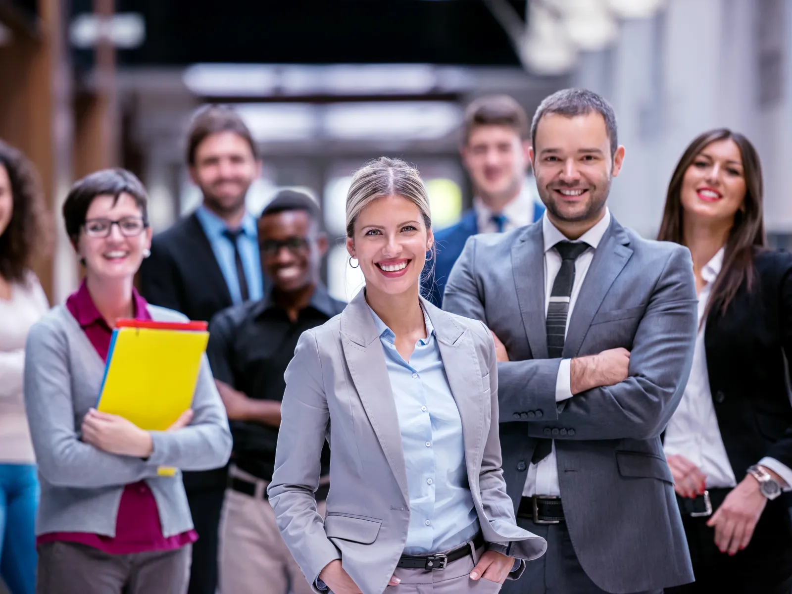 Diverse professional team in business attire smiling confidently in office corridor