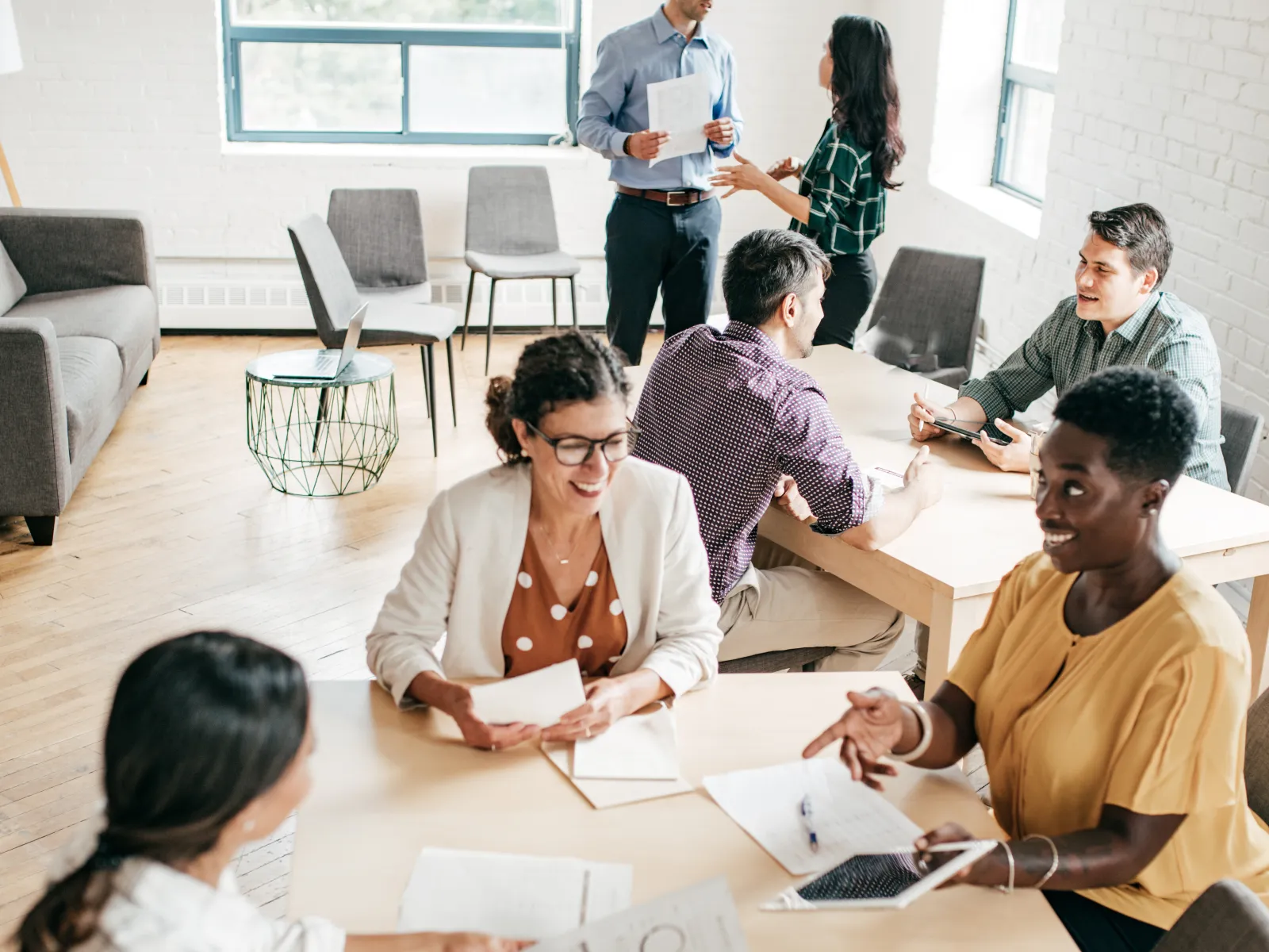 Diverse group of professionals collaborating in a bright, modern office around tables and discussing documents and ideas.