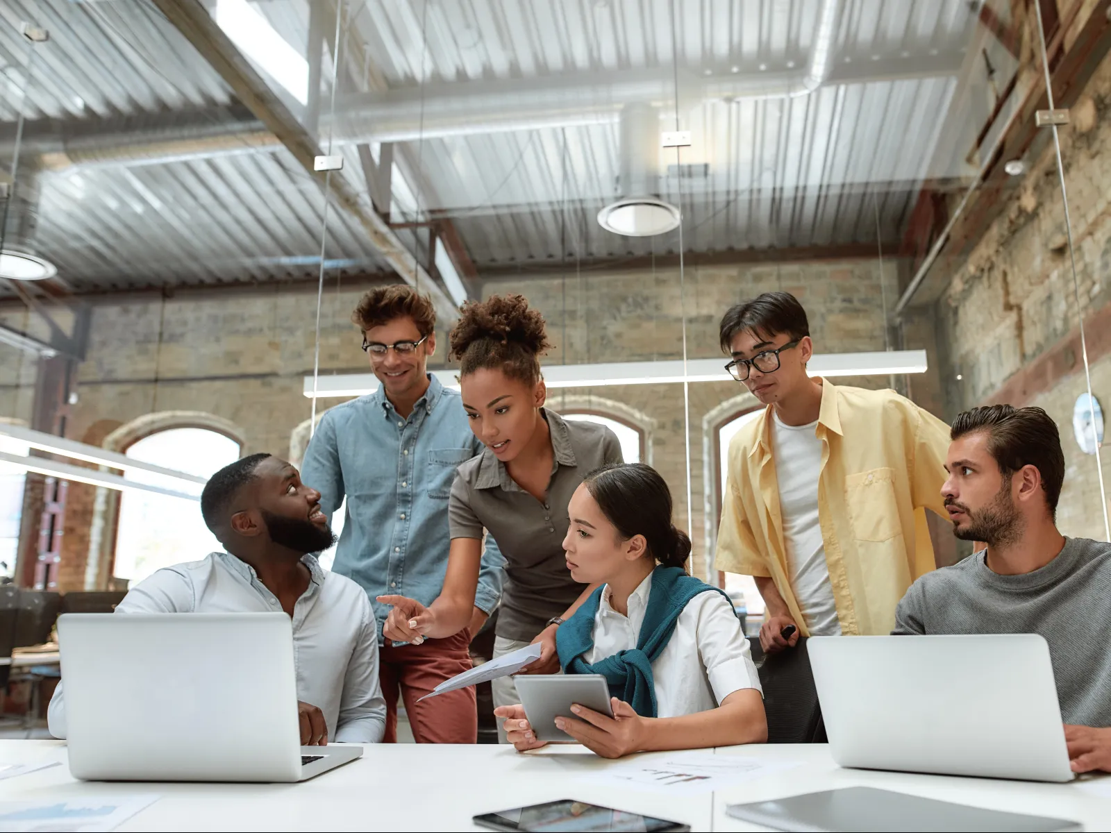 Diverse group of young professionals collaborating around laptops in modern open office space, discussing a project.