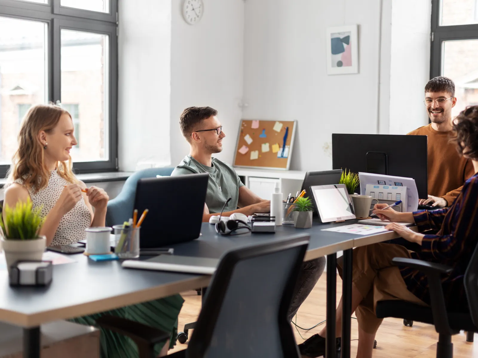 Team of four professionals collaborating in a bright modern office with laptops and digital devices.