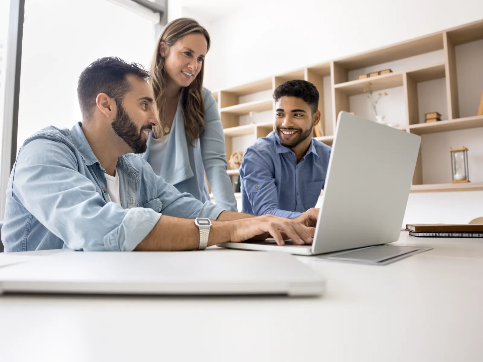 Three young professionals collaborating and smiling while working on a laptop in a modern office setting