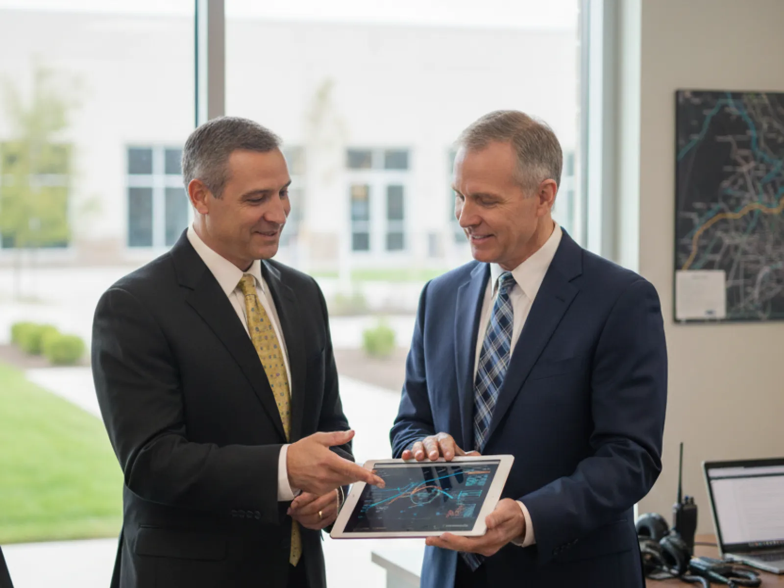 Two businessmen in suits discussing a digital tablet with charts in a modern office setting.