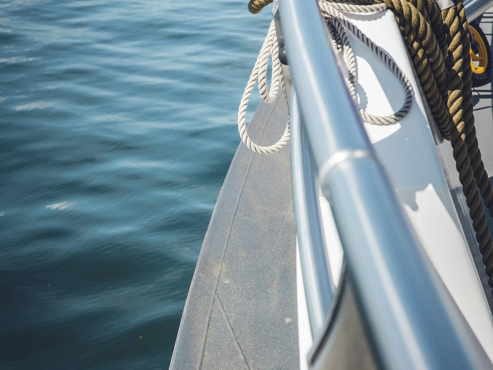 Coiled ropes secured on the railing of a boat with calm blue water in the background under bright daylight.