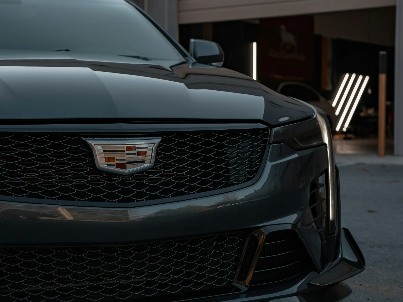 Front view of a sleek black Cadillac car parked outside a garage with modern lighting.