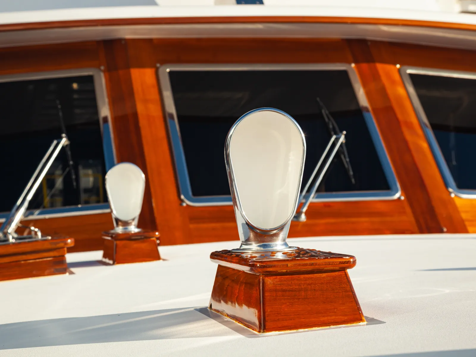 Polished wood and chrome boat cleats on a white deck with wooden cabin windows and windshield wipers.