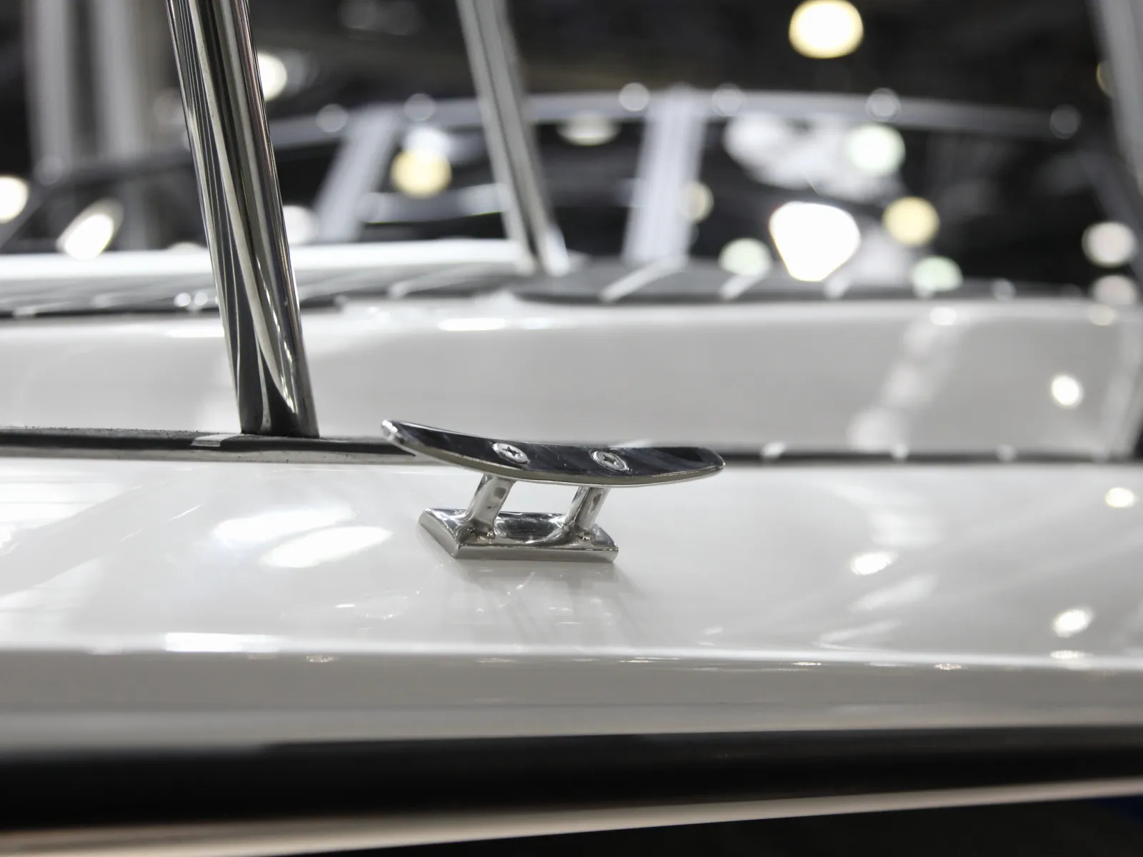 Close-up of a metal cleat on a white yacht deck with blurred lights in the background.