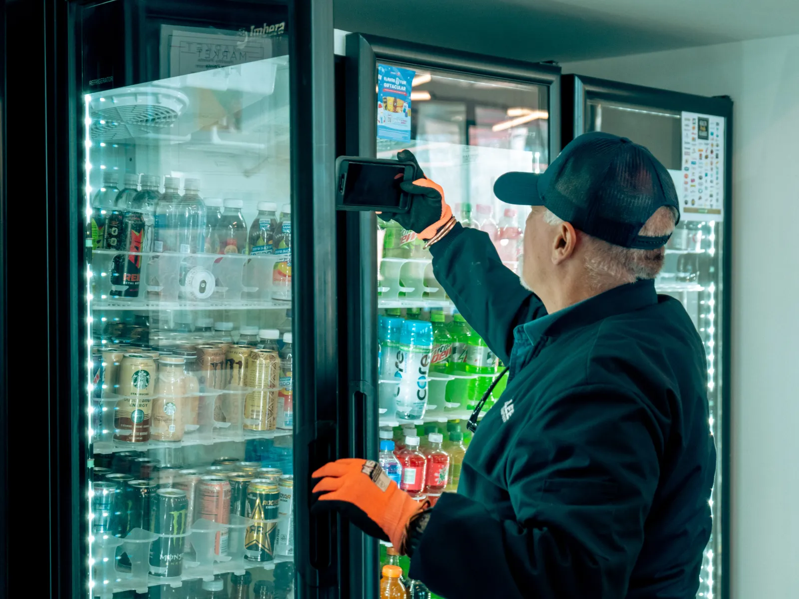 a man in a blue hat holding a camera in front of a refrigerator