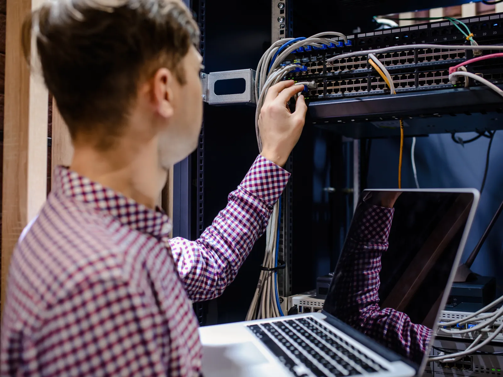 Technician working on server rack cables with laptop in data center environment