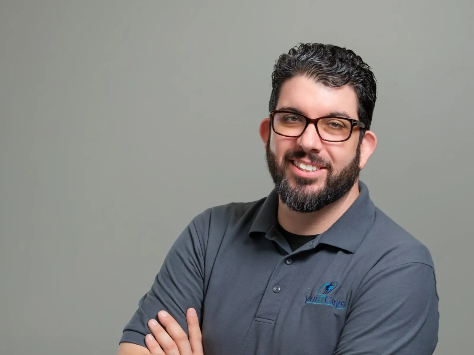 Smiling man with glasses and beard wearing a gray polo shirt with YouthGuys logo on a gray background.