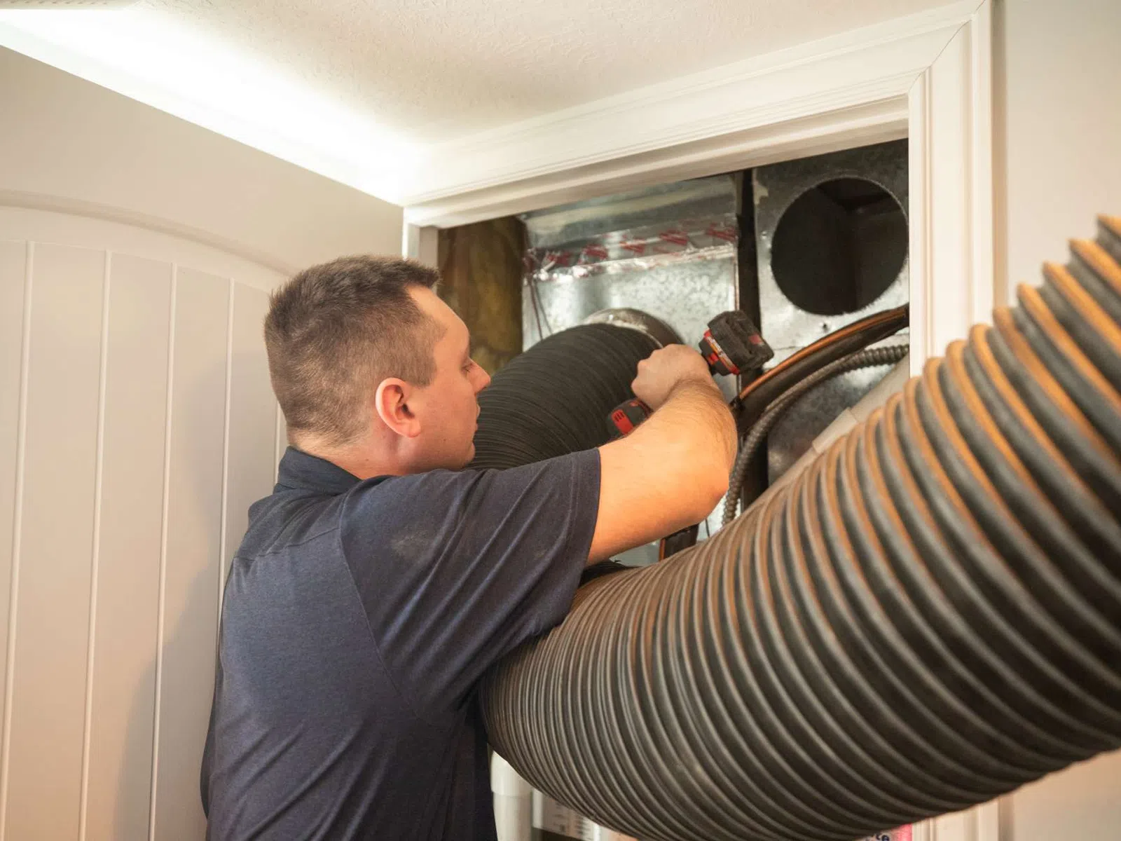 Technician installs or repairs large flexible ducting in HVAC system inside building interior.