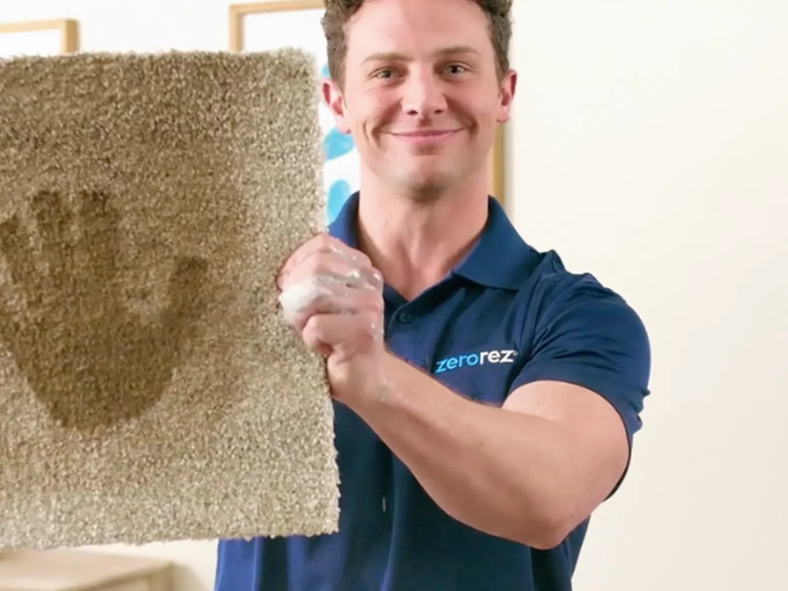Man in blue shirt demonstrating a clean carpet square with a visible clean handprint in a home setting.