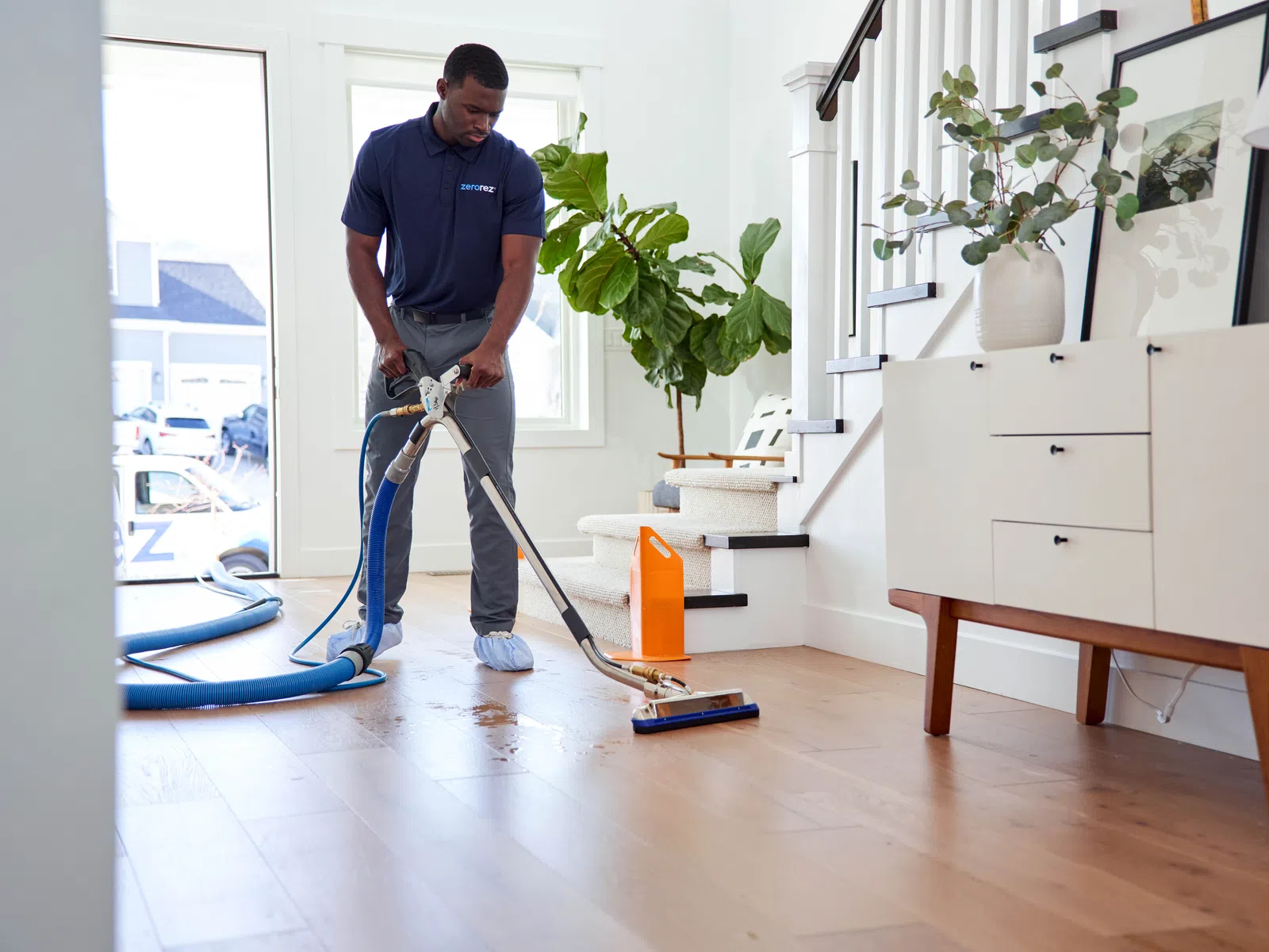 A person cleaning hardwood floors using a vacuum in a bright, modern home interior.
