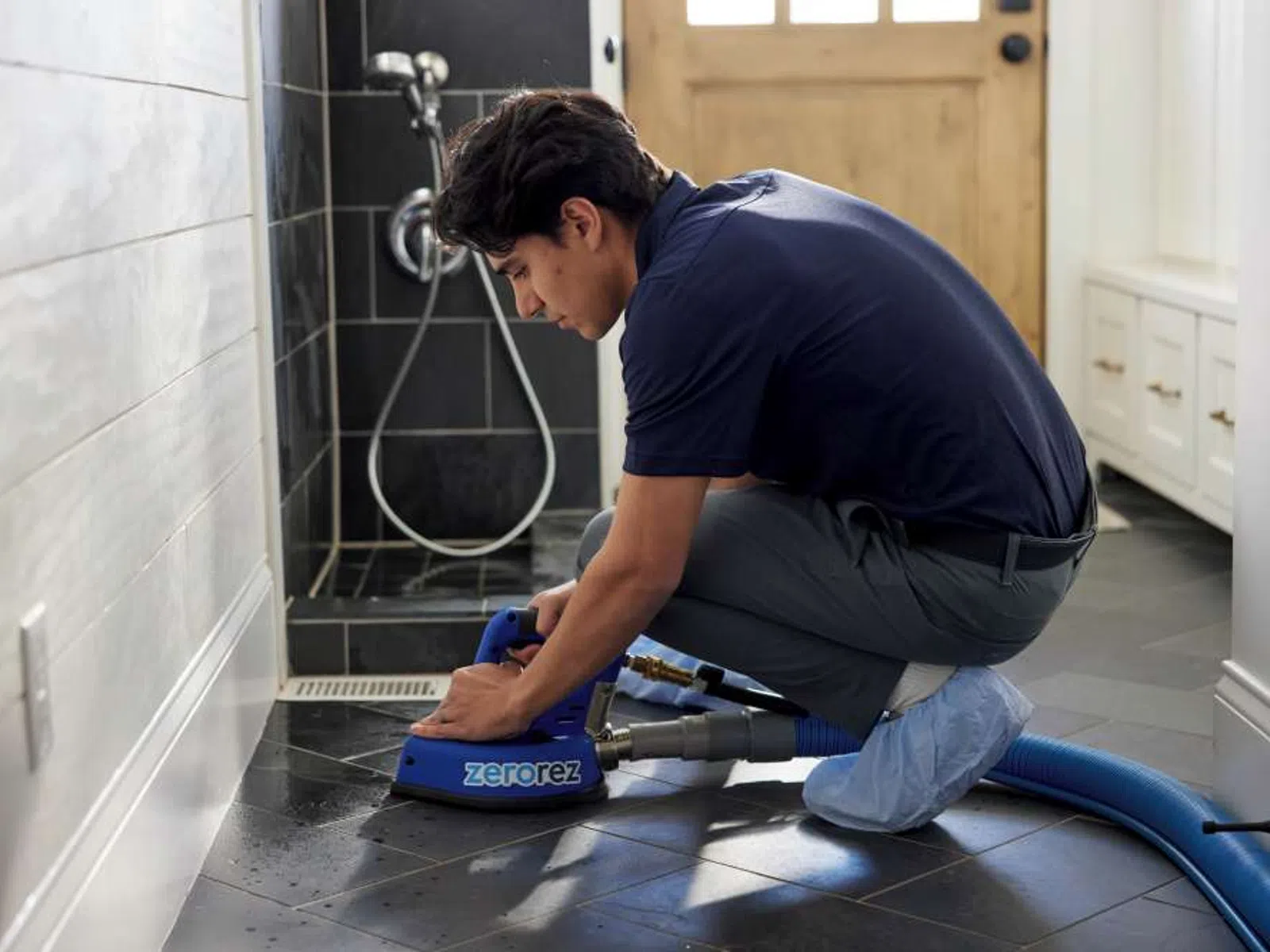 Technician cleaning black tiled floor in a bathroom using Zerorez cleaning machine and hose.