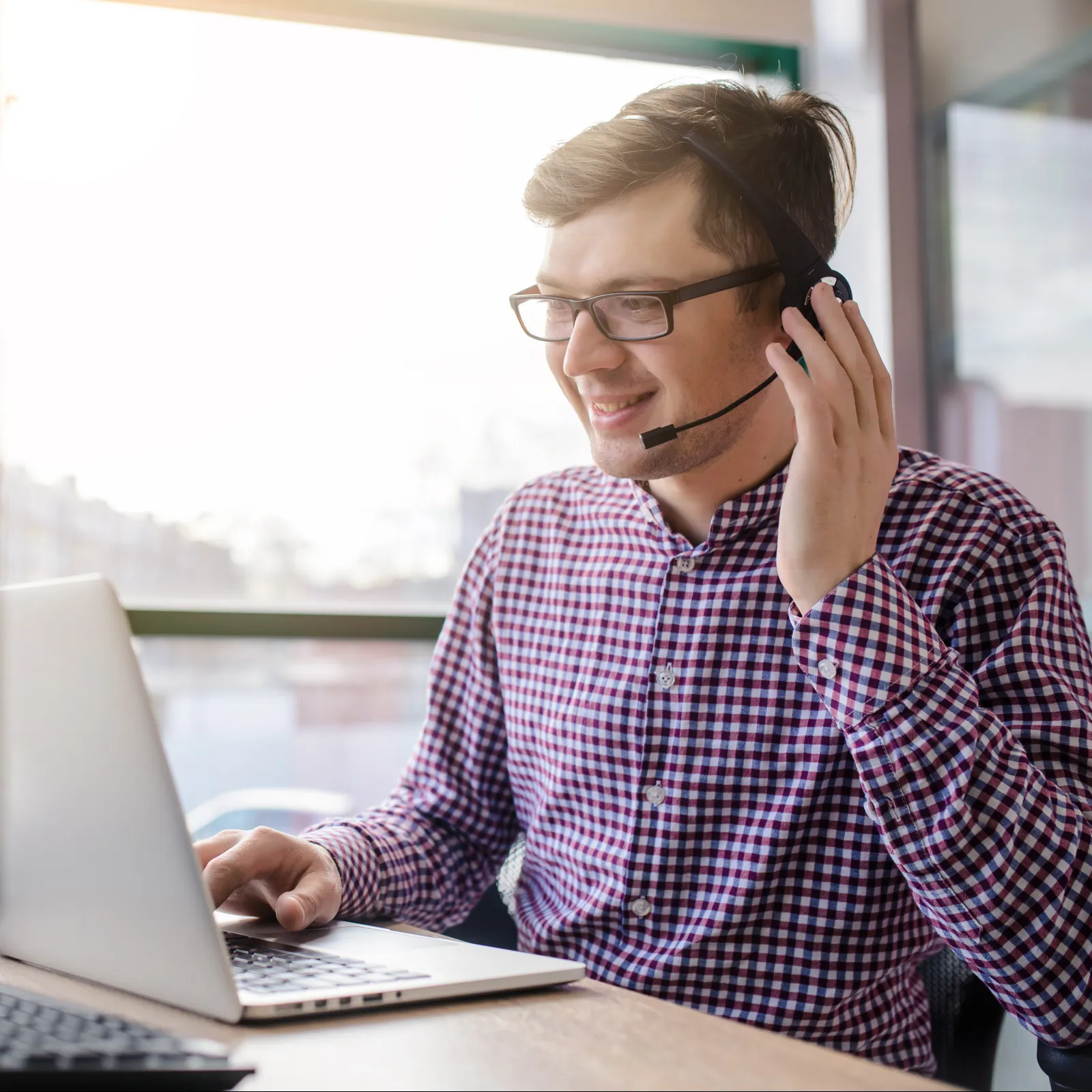Man with a headset working on a laptop in a modern office, engaged in a conversation.