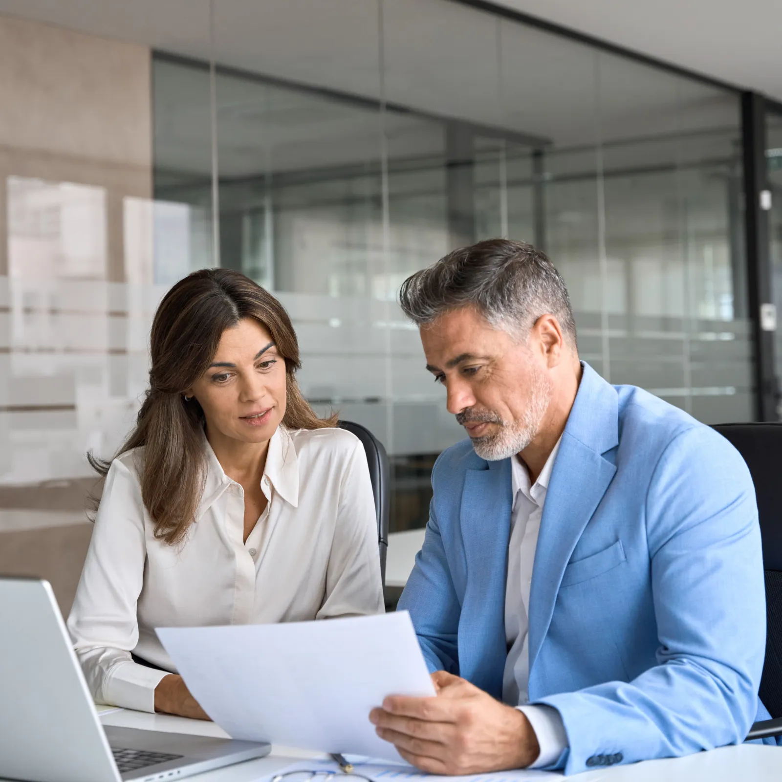 Business professionals discussing documents in a modern office setting with a laptop on the desk.