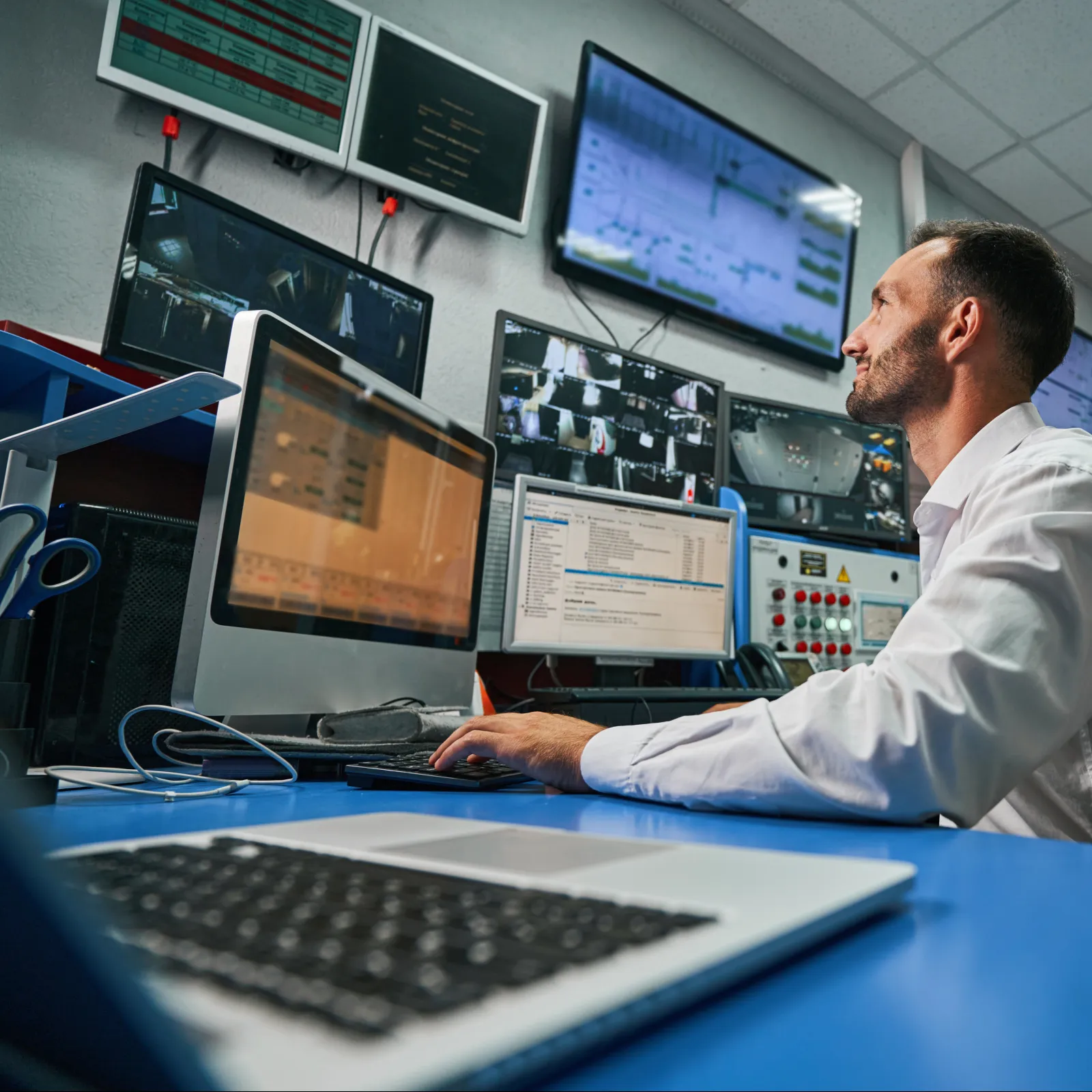 Professional man working at a computer in a control room with multiple screens and equipment.