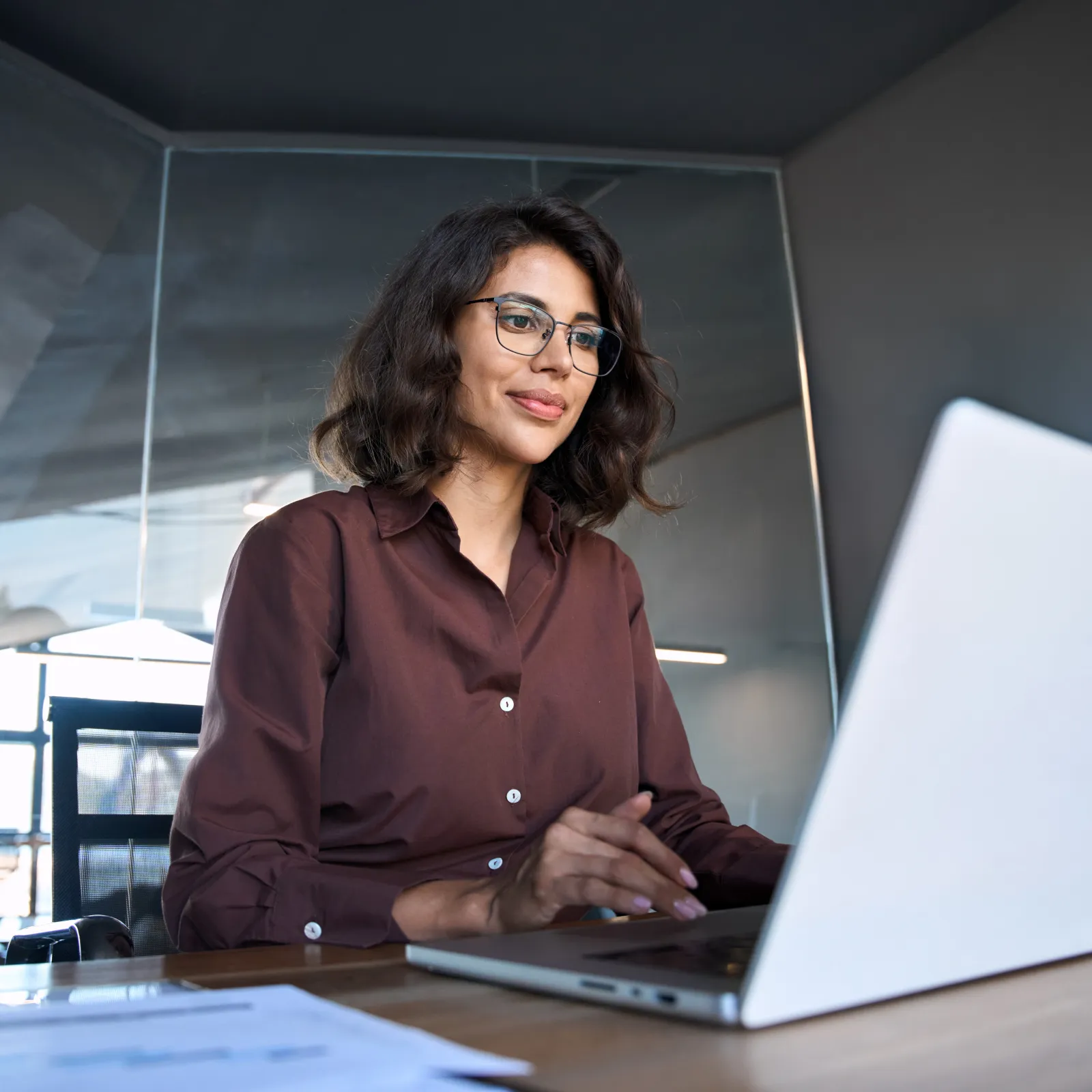 Professional woman working on a laptop in a modern office environment with natural light.