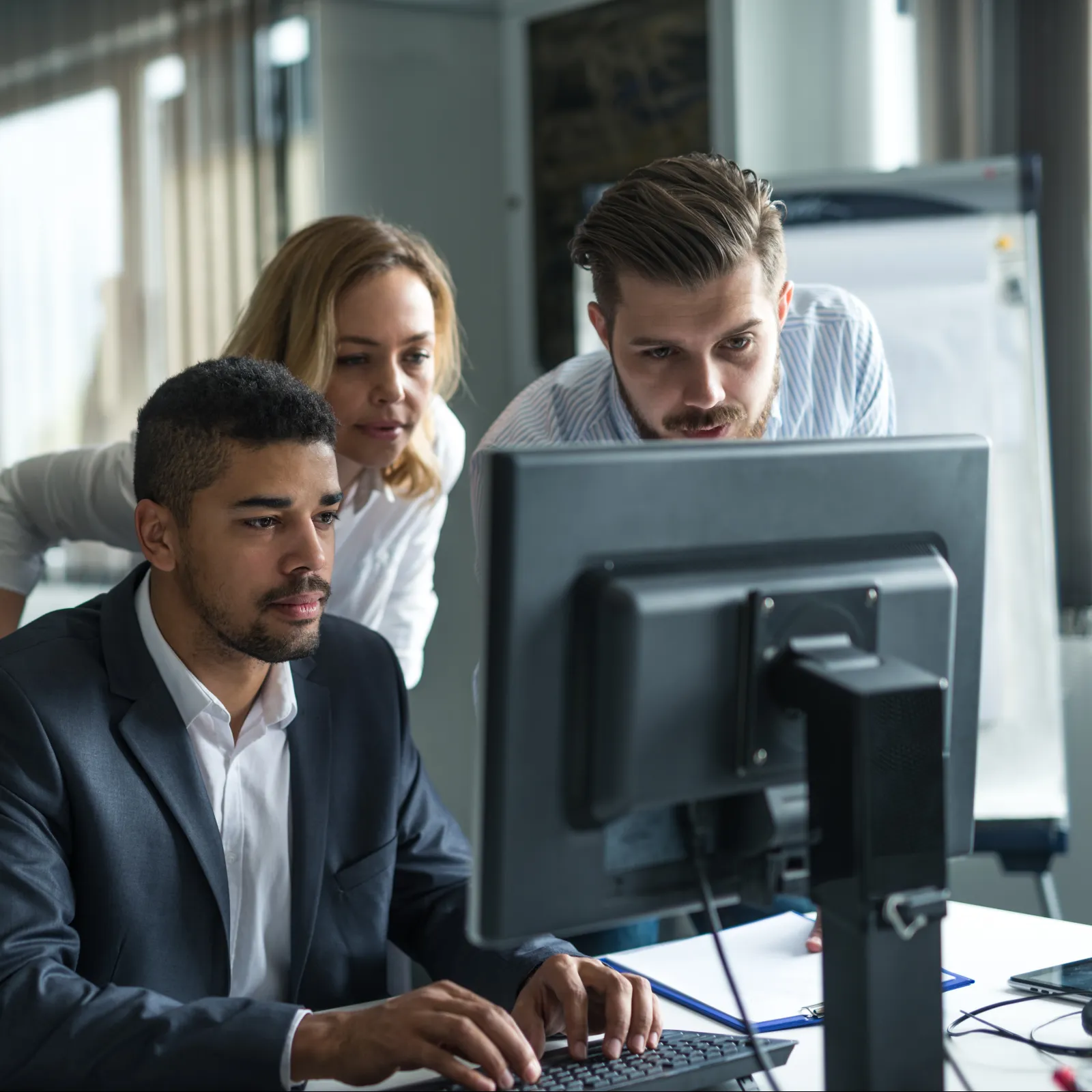 Three professionals collaborating in an office setting, focused on a computer screen.