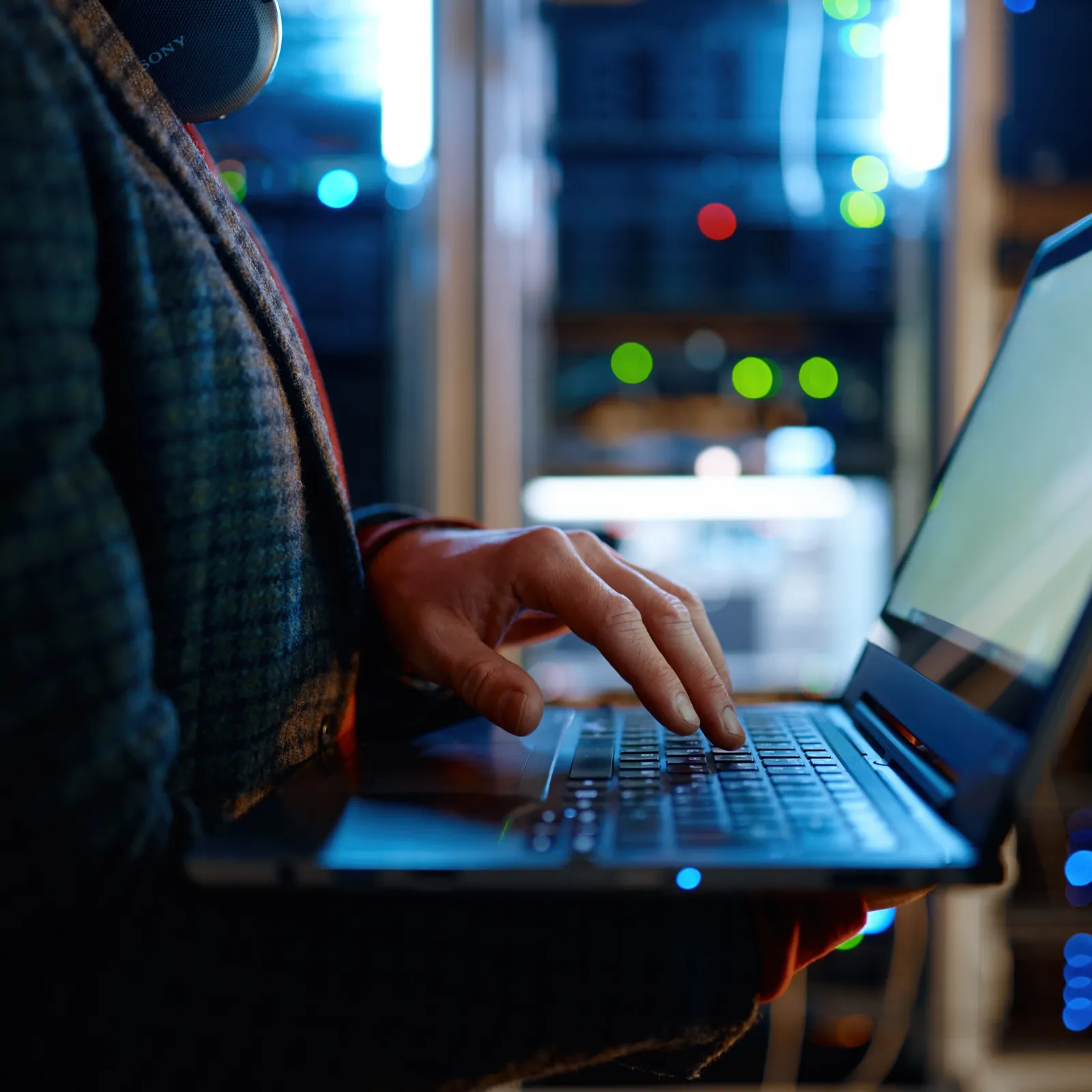 A person typing on a laptop in a data center with illuminated server racks in the background.