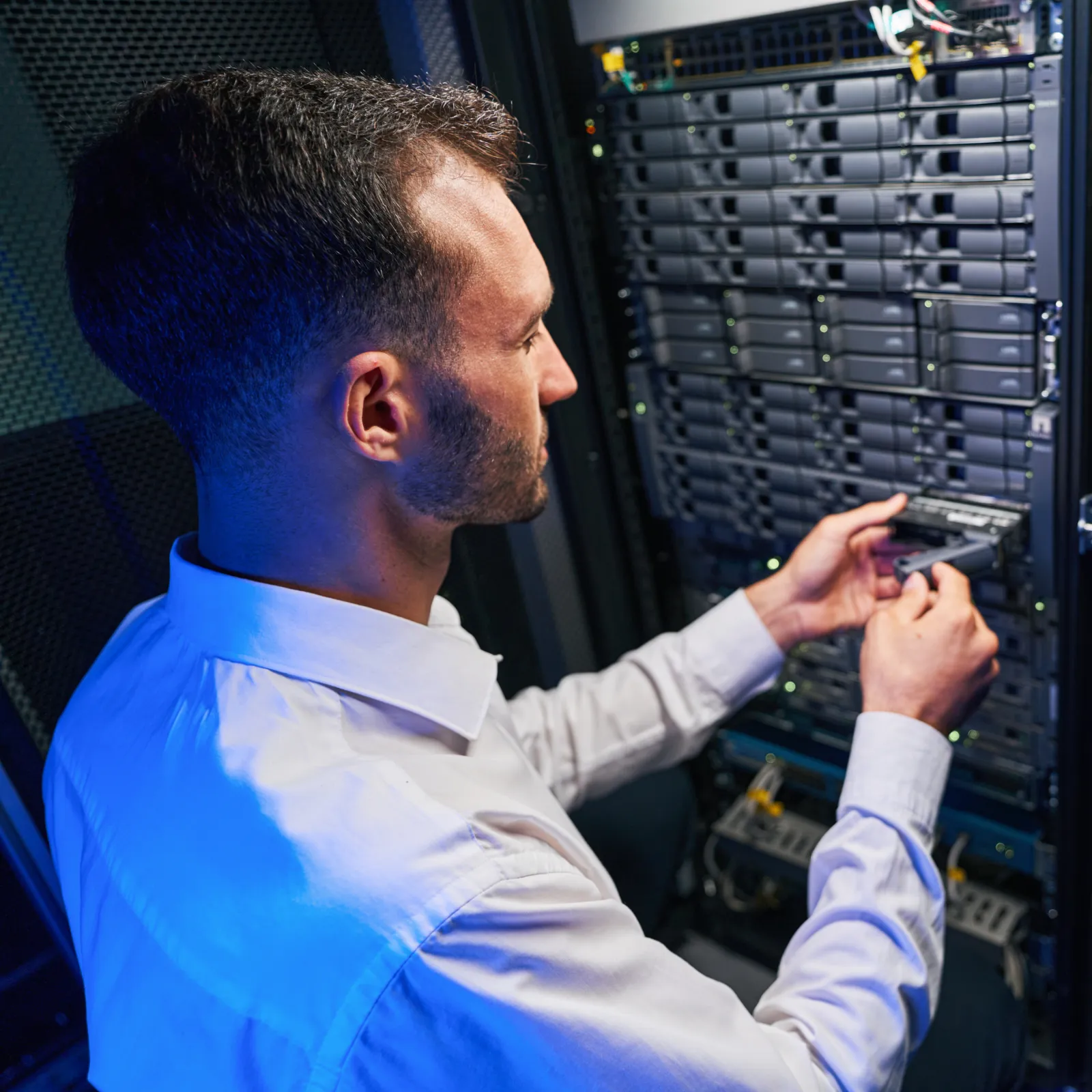 Technician working on a server rack, focused on hardware maintenance with blue lighting.