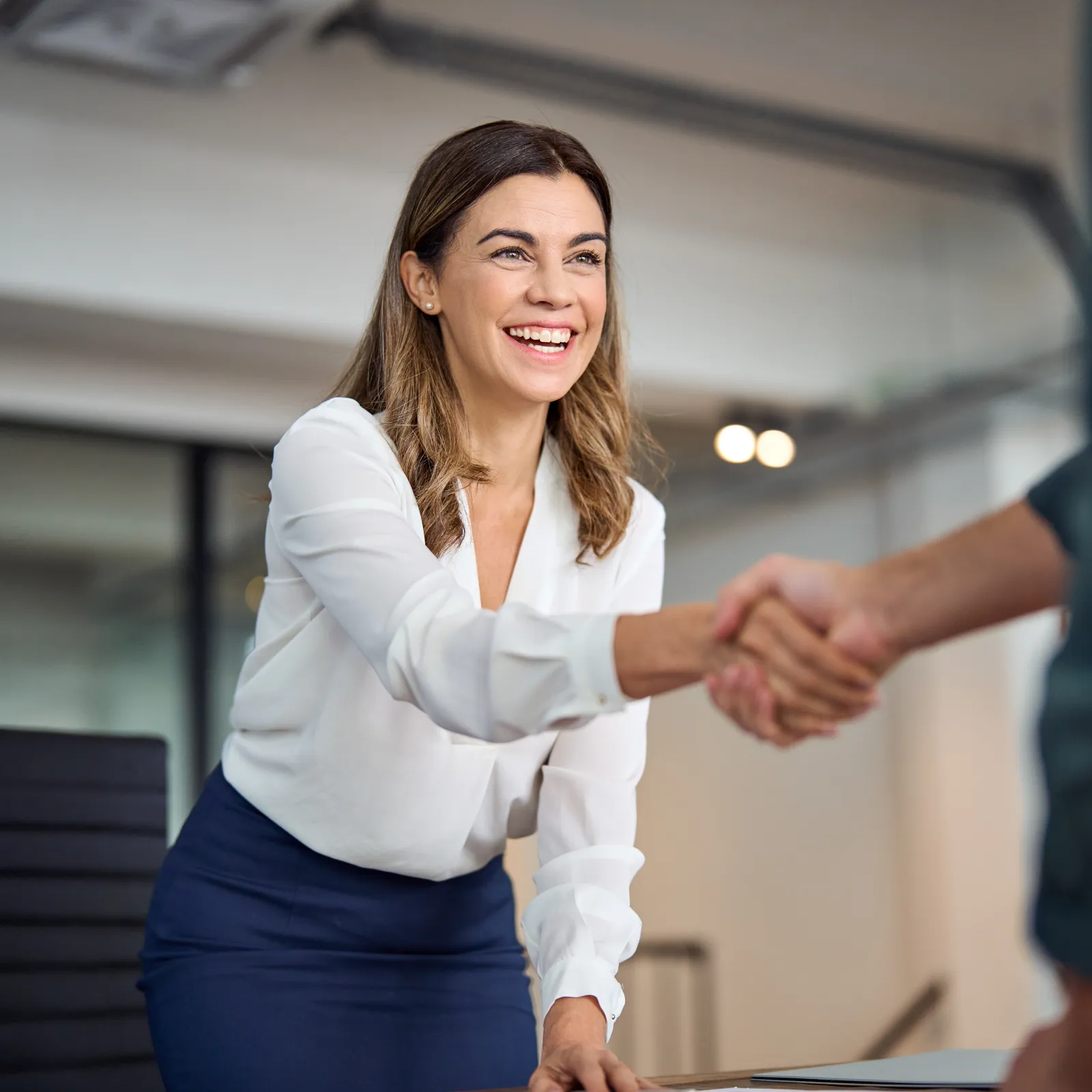 A woman smiling and shaking hands in a modern office setting, showcasing a positive business interaction.