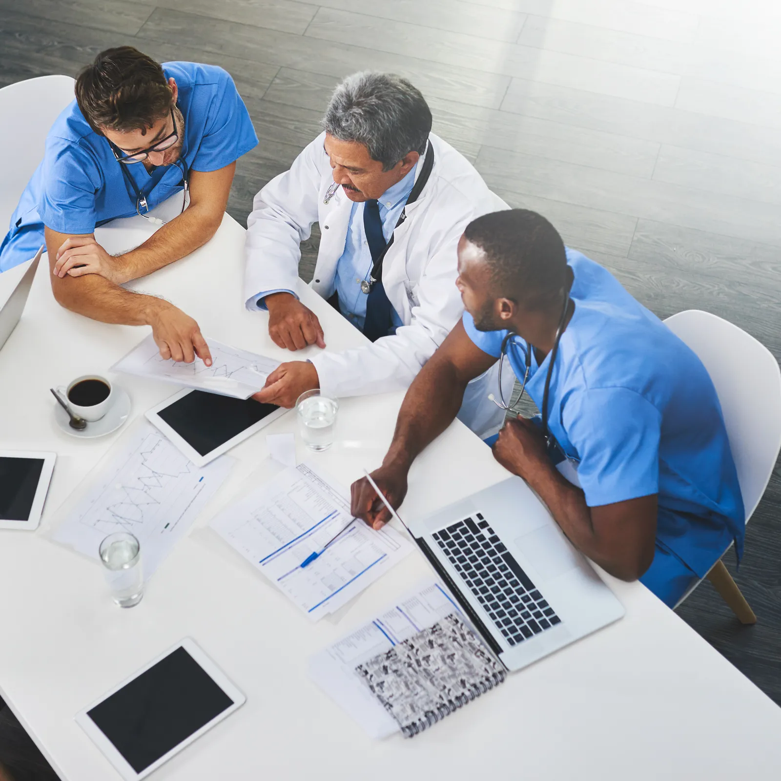 Healthcare professionals collaborate at a table with devices and documents, sharing ideas in a bright office.