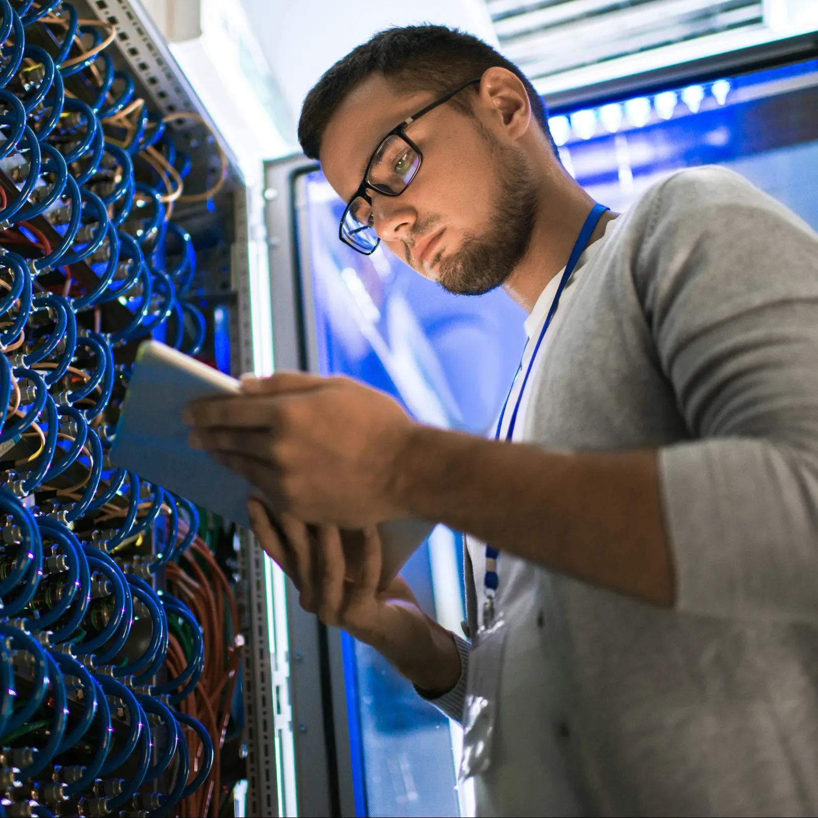 A technician checks data cables and connections in a server room with blue lighting.