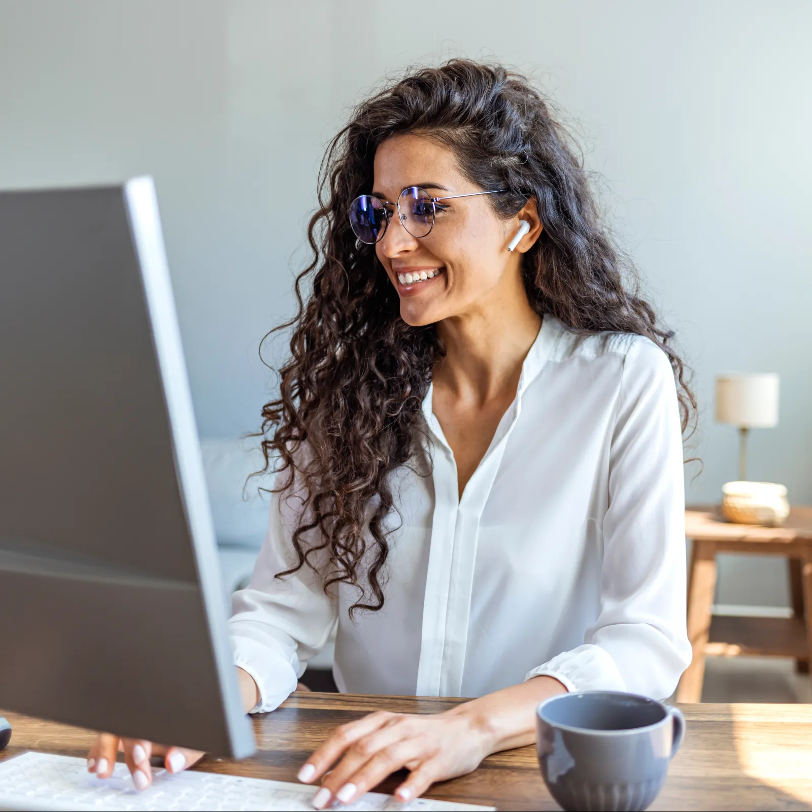 Smiling woman working on a computer in a bright home office with plants and stylish decor.