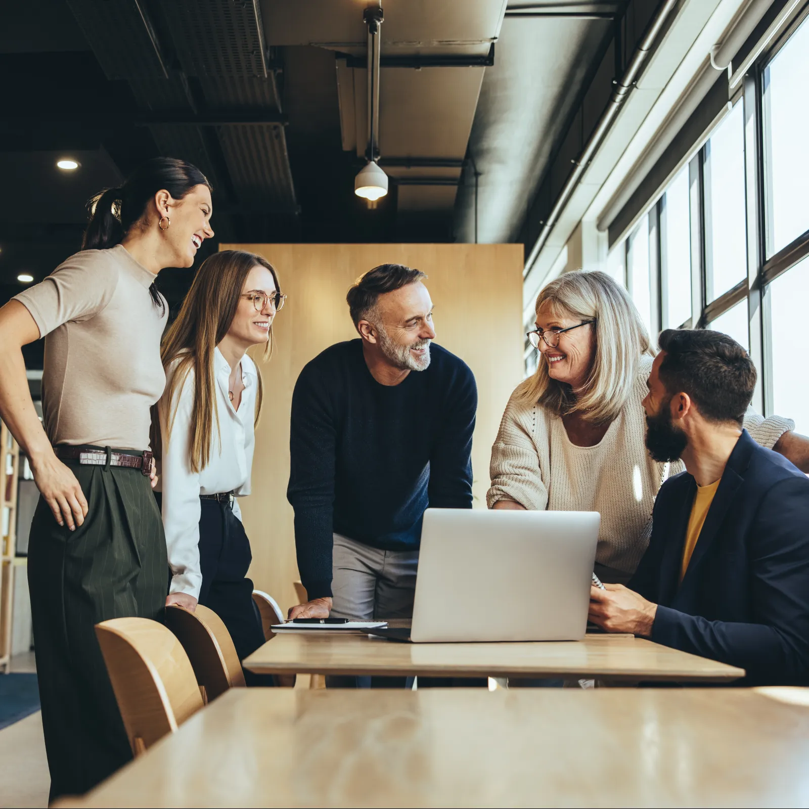 Group of professionals collaborating in a modern office setting, discussing ideas over a laptop.