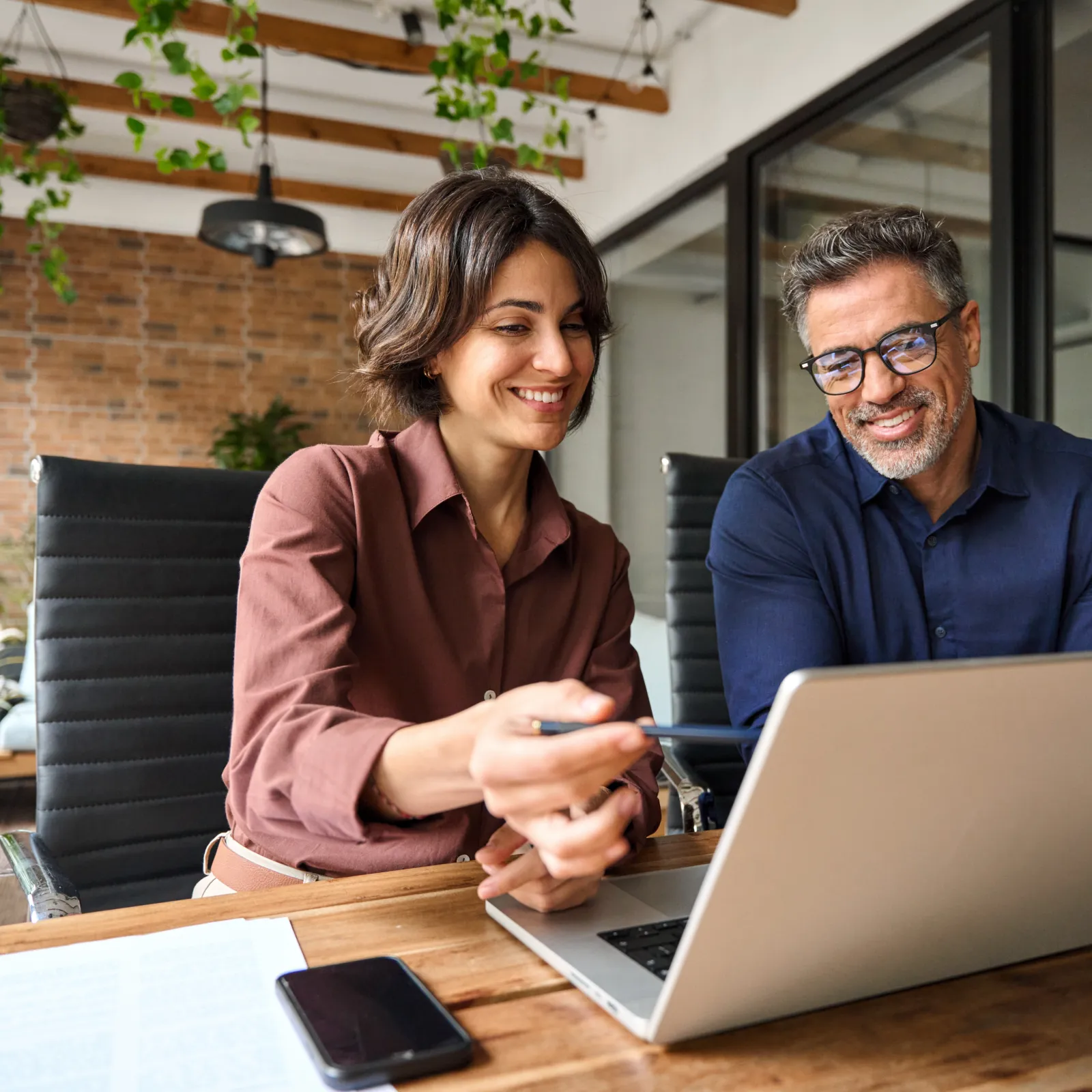 Two professionals collaborating at a modern office, smiling and discussing over a laptop.