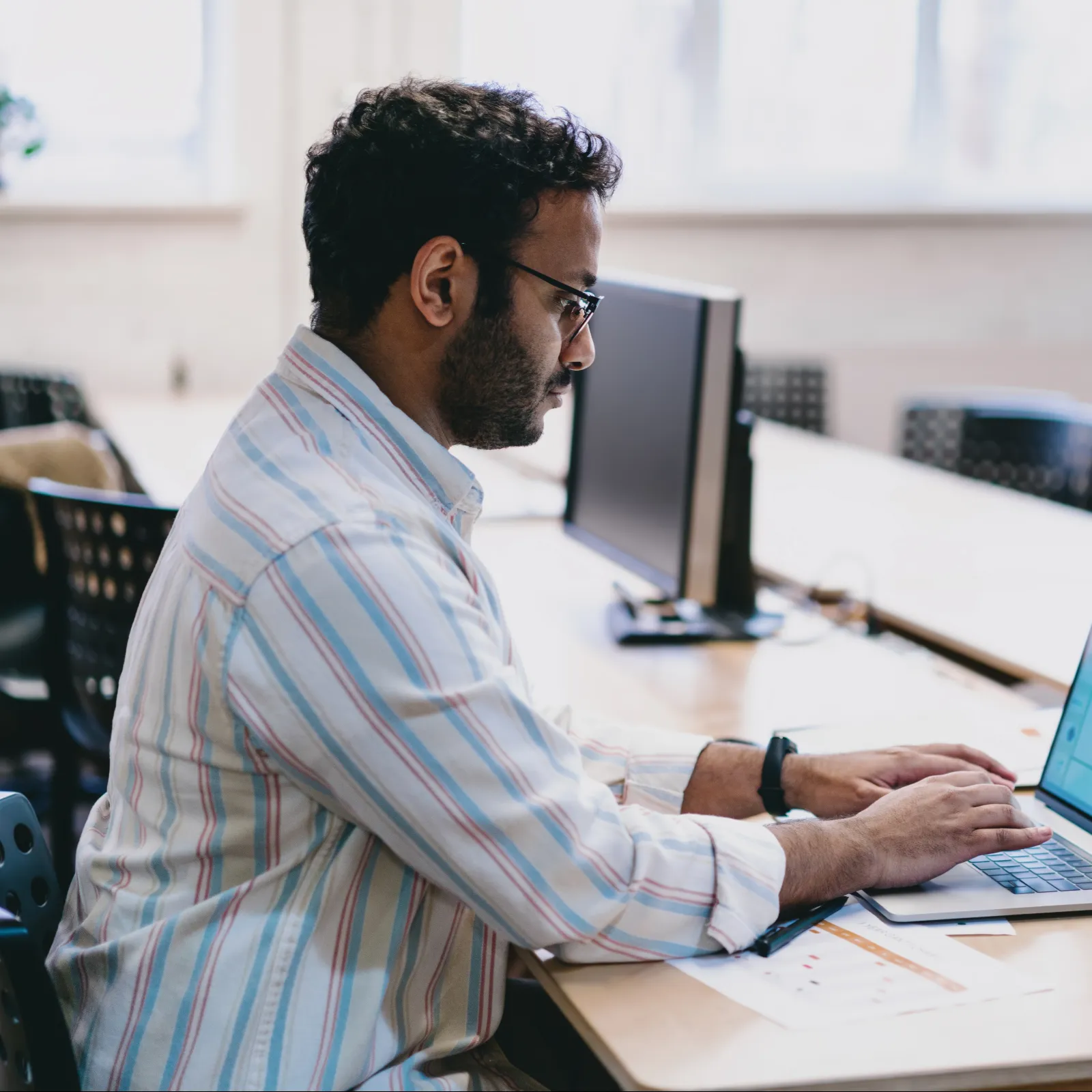 A focused man working on a laptop in a modern office setting with minimalist decor.
