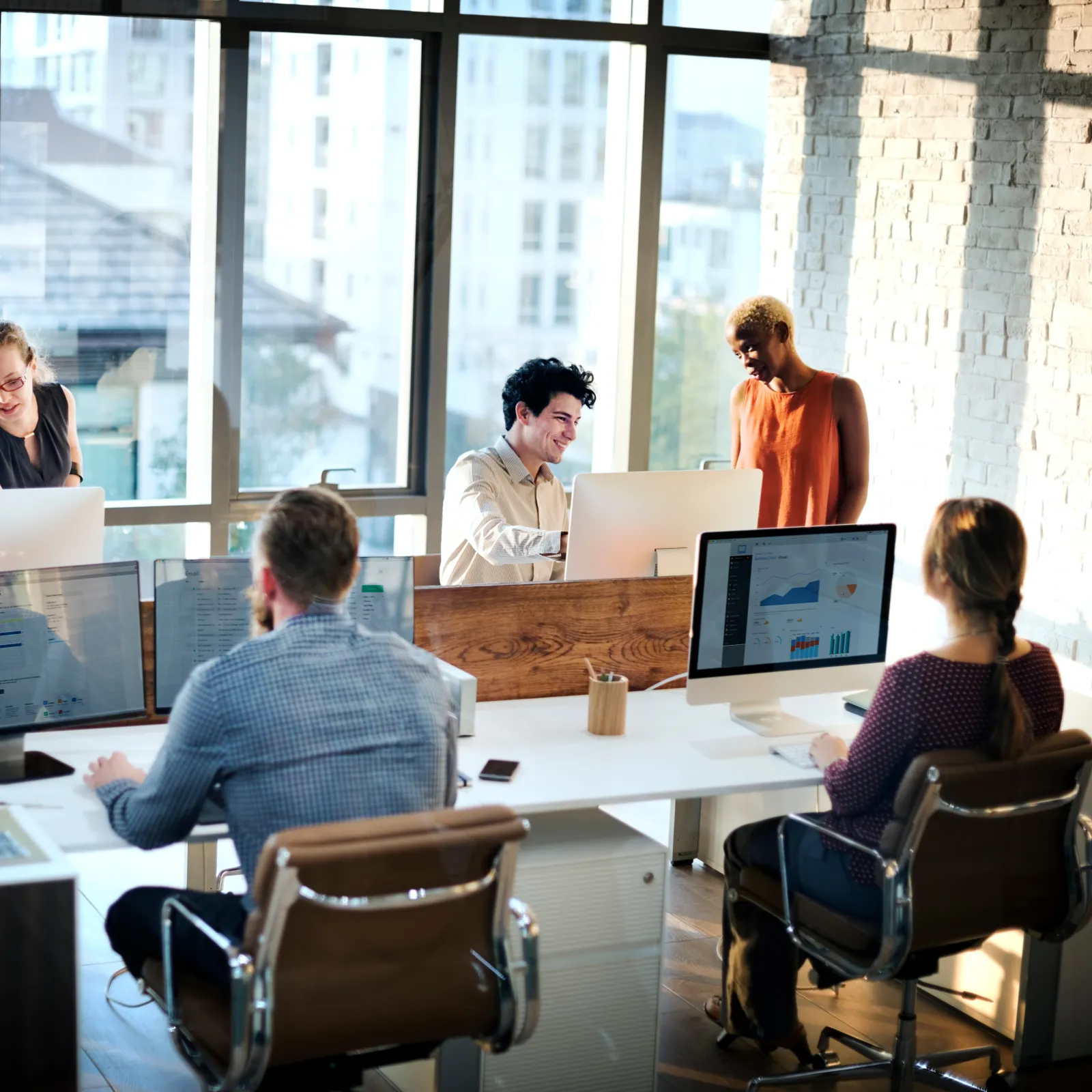 Collaborative office scene with professionals engaged in discussion and working at computers.