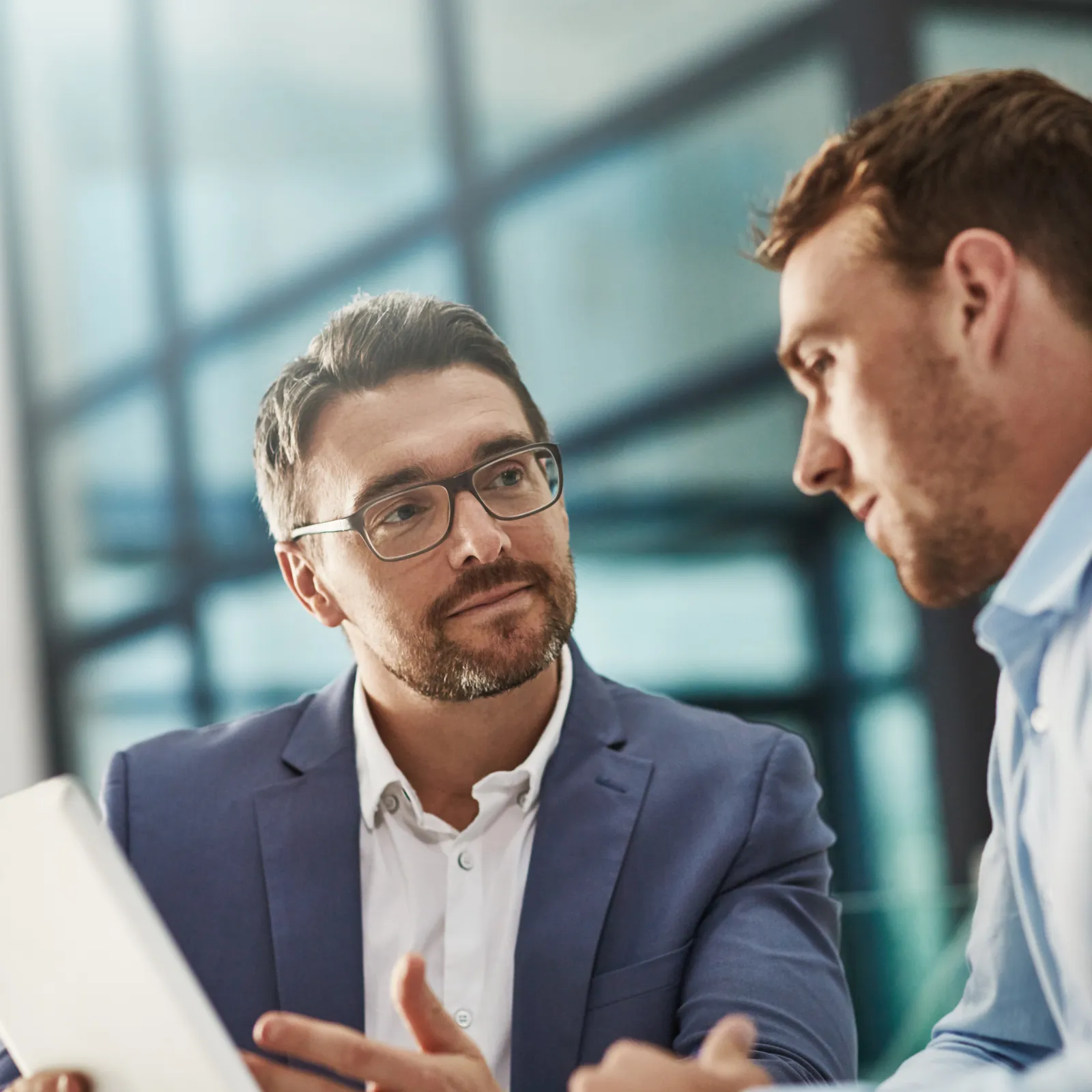 Two professionals engaged in a discussion in a modern office setting with a tablet.