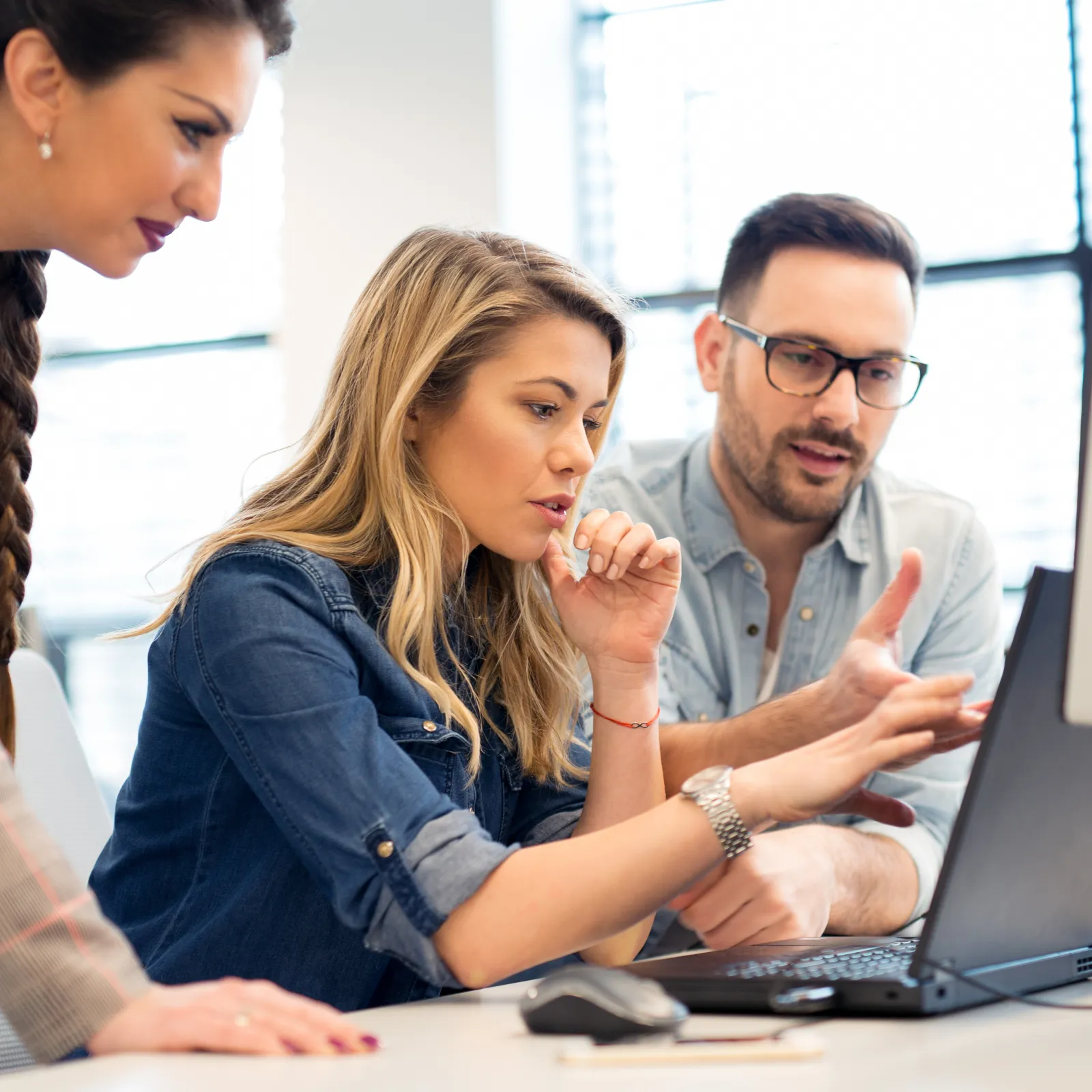 Three colleagues collaborate on a project, analyzing data on a computer screen in a modern office setting.