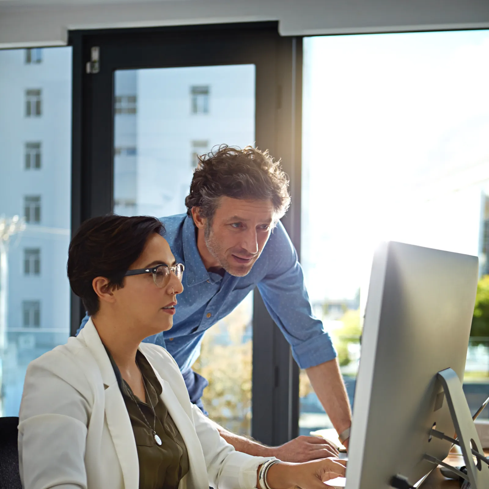 Professional colleagues collaborate at a desk with a computer in an office setting.