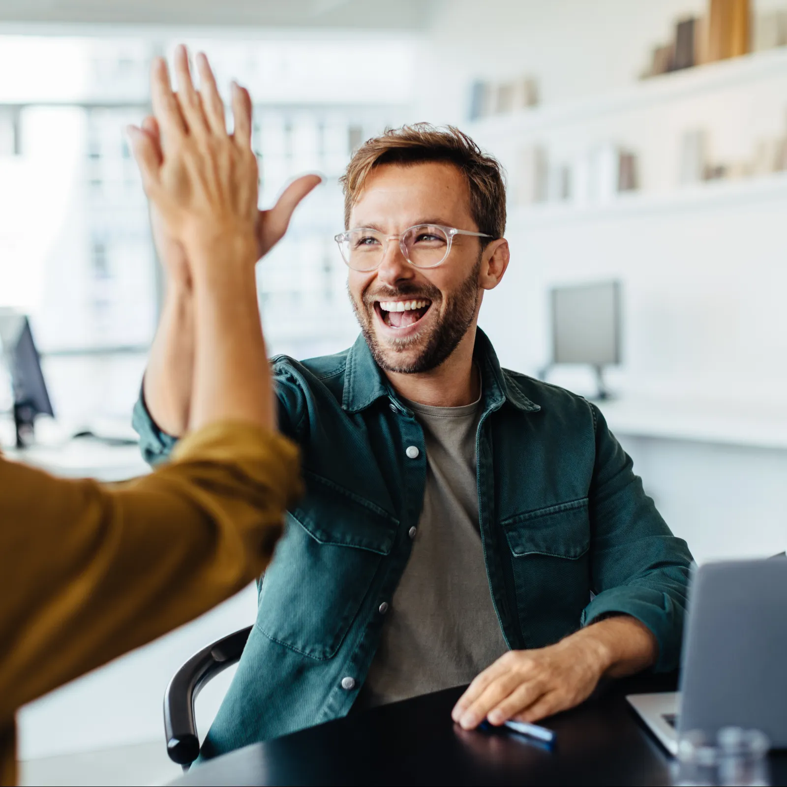 Three professionals collaborating and celebrating success in a modern office setting.