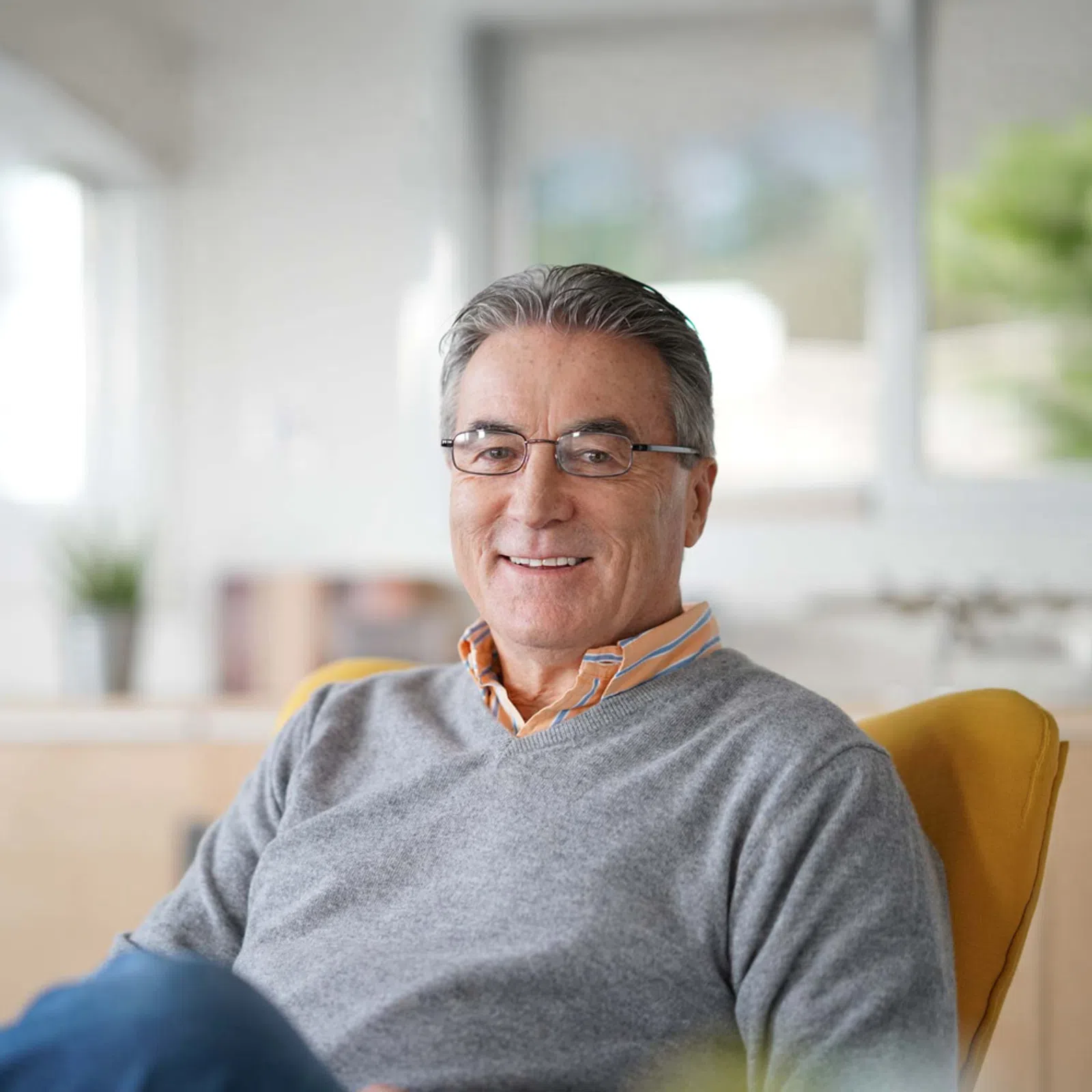 Smiling middle-aged man wearing glasses and grey sweater sitting comfortably in a bright modern office.