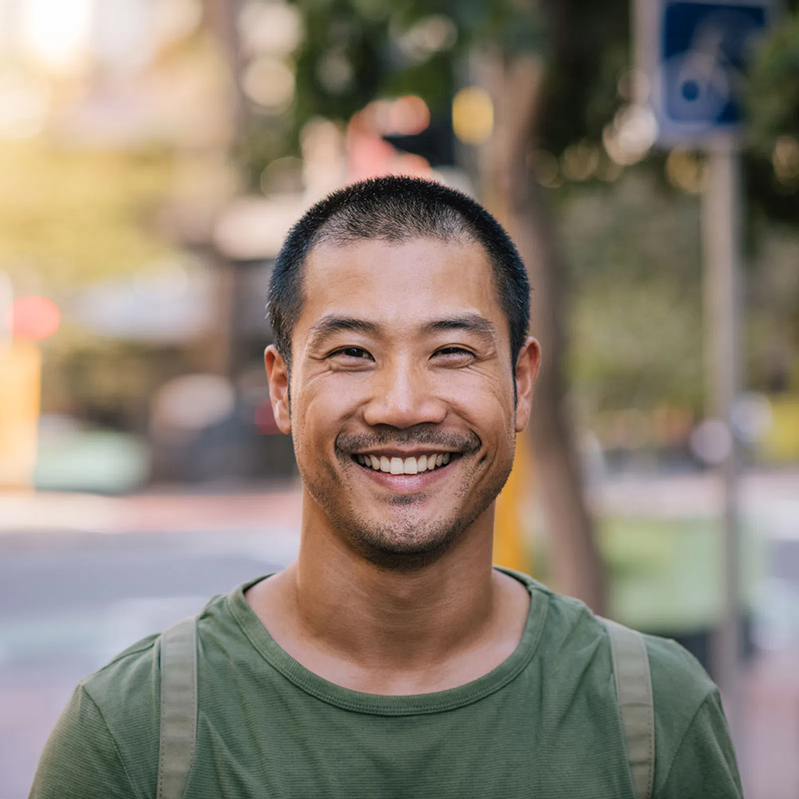 Smiling young man with short hair wearing green shirt standing outdoors on city street during daytime
