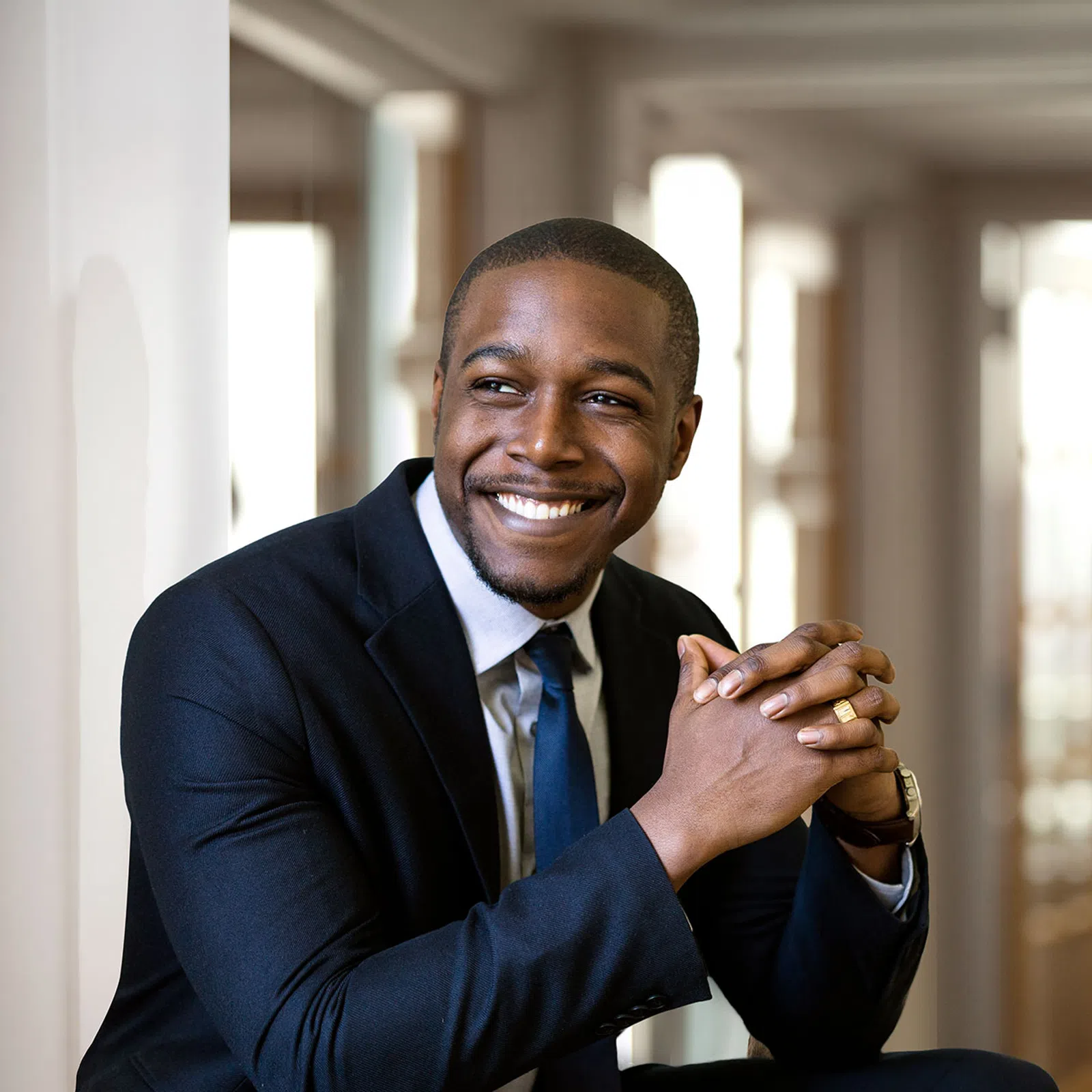 Smiling African American businessman in suit sitting with hands clasped in bright modern office space.