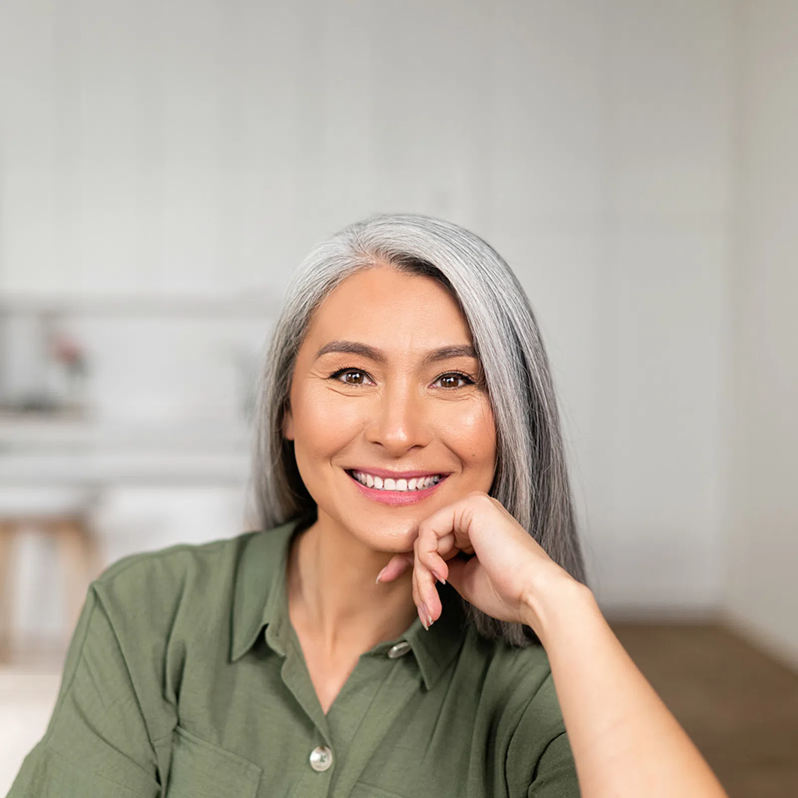 Smiling middle-aged woman with gray hair wearing green shirt in a bright modern kitchen.