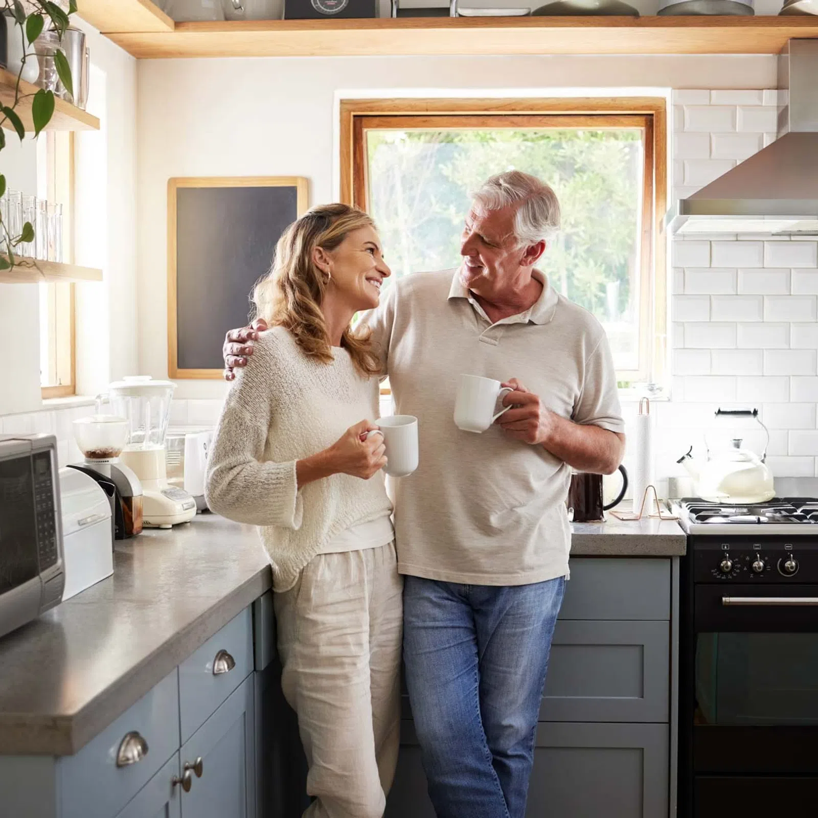 Smiling middle-aged couple drinking coffee and embracing in a modern kitchen with natural light.