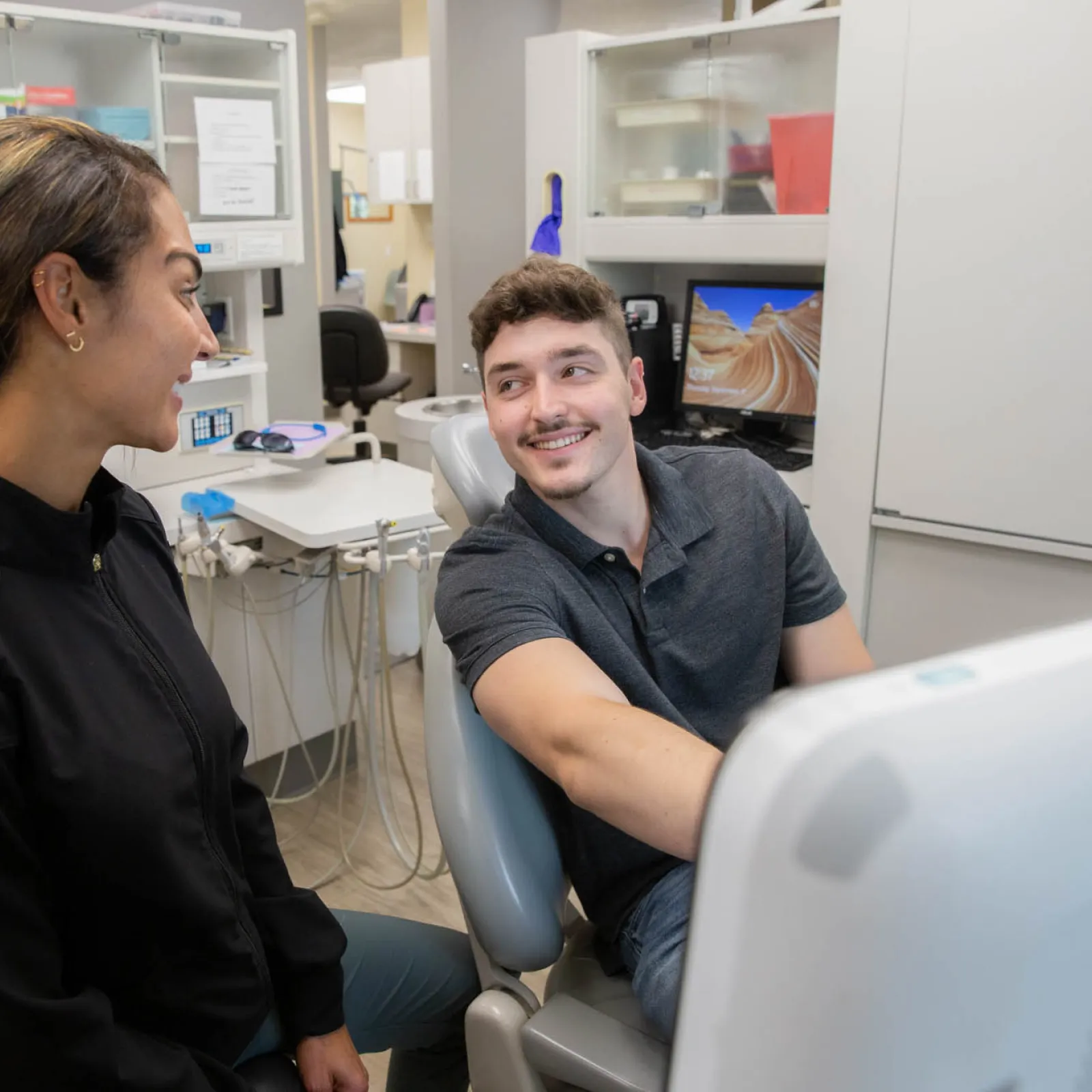 Male patient and female dental hygienist smiling and talking in a modern dental office setting.