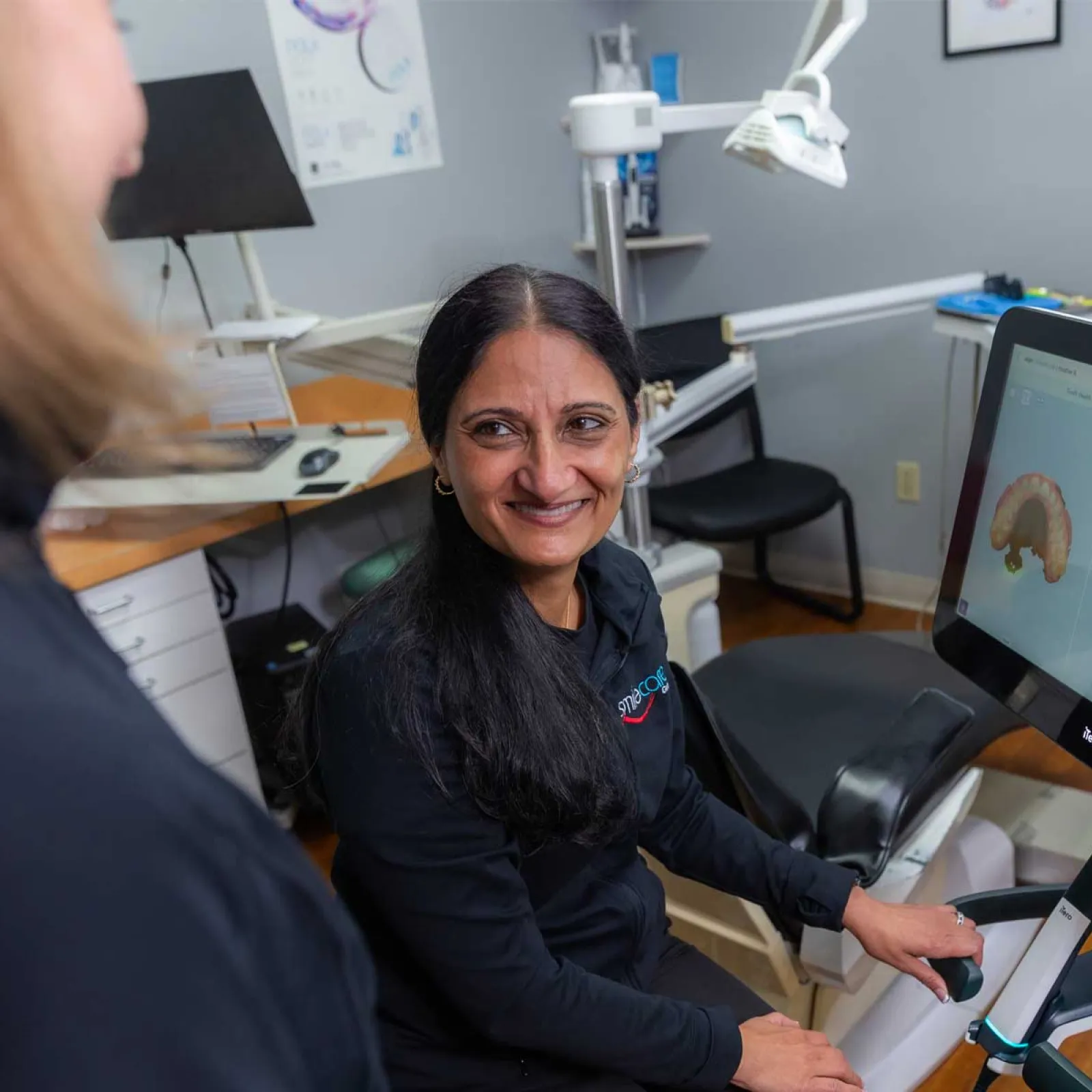 Dental professional using digital scanning equipment with 3D tooth models displayed on a monitor in clinic.