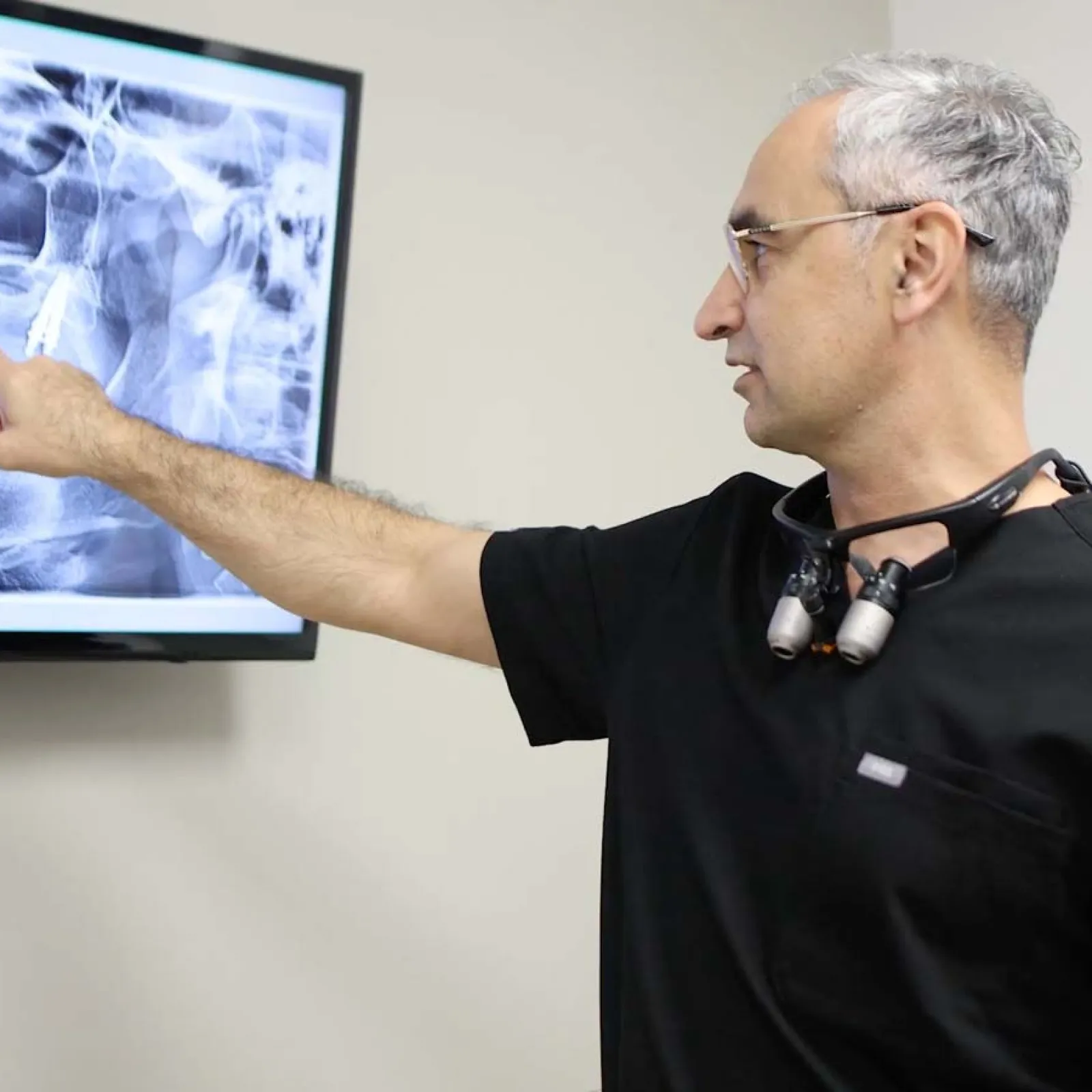 Dentist in black scrubs pointing at dental X-ray with implants displayed on monitor in clinic.